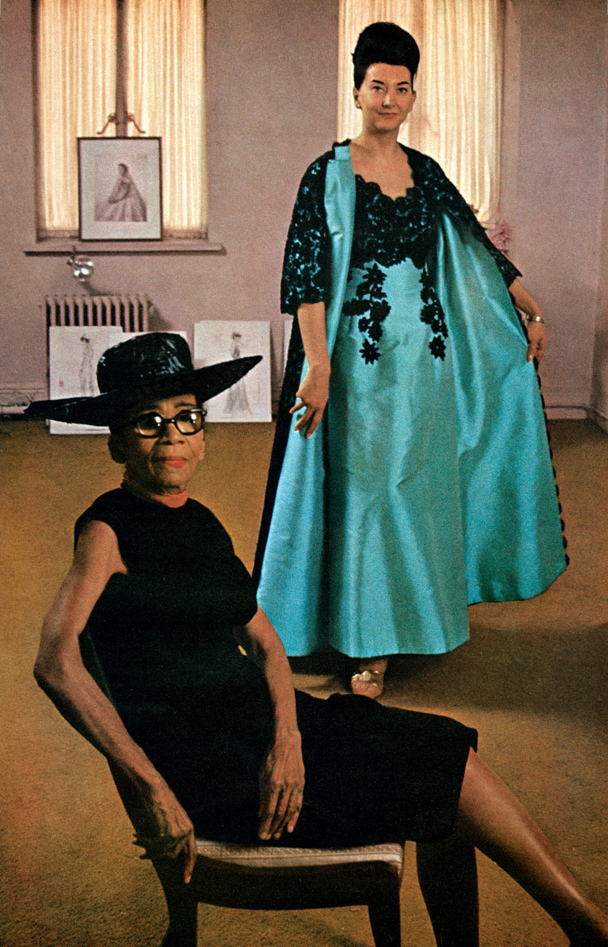 Ann Lowe, Dean of fashion designers, is photographed in her New York salon with London model Judith Palmer, wearing Lowe theater gown and coat of Italian Mecado silk, with black lace reembroidered in black soutache.