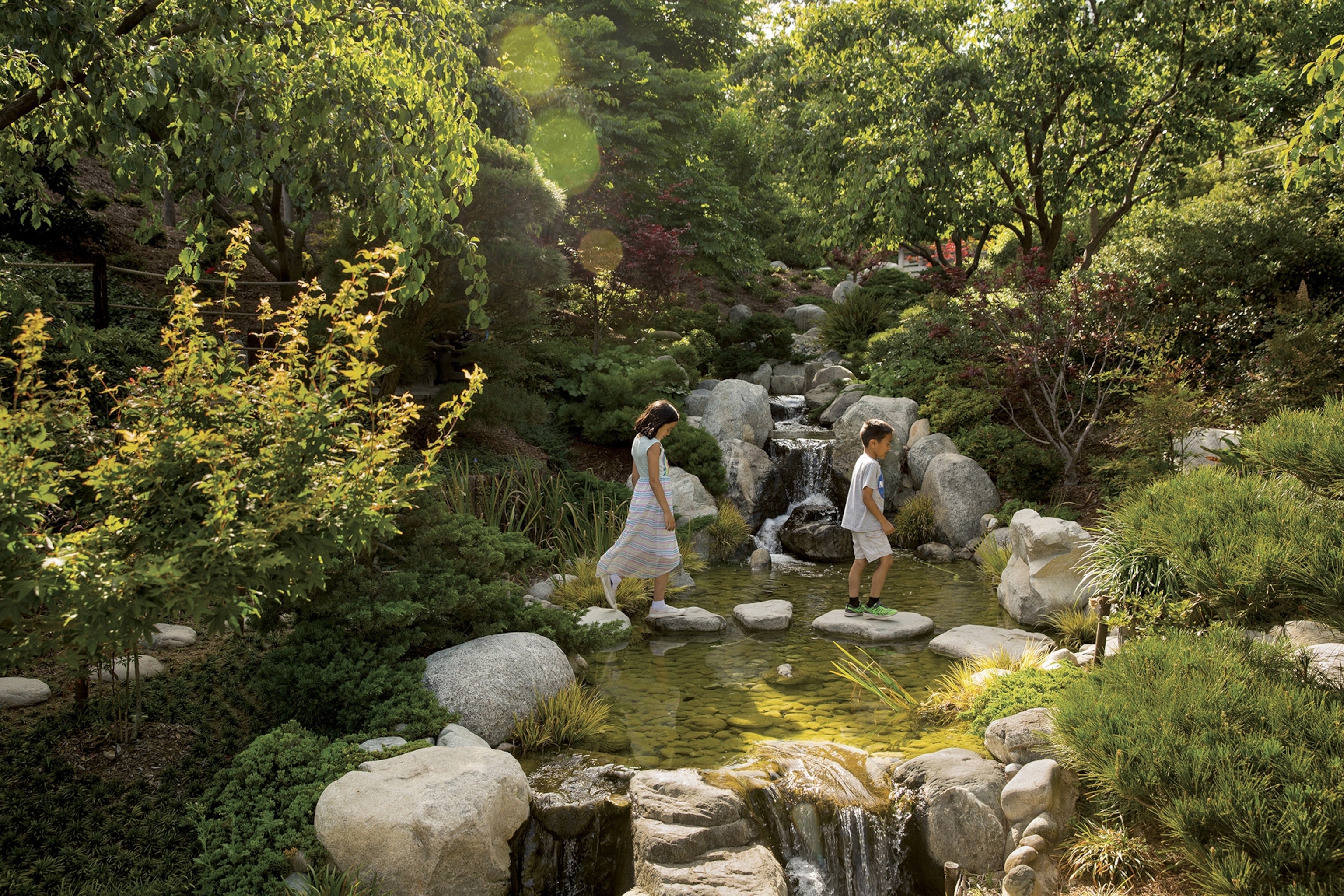 Two children walk over stepping stones at the Japanese Friendship Garden.