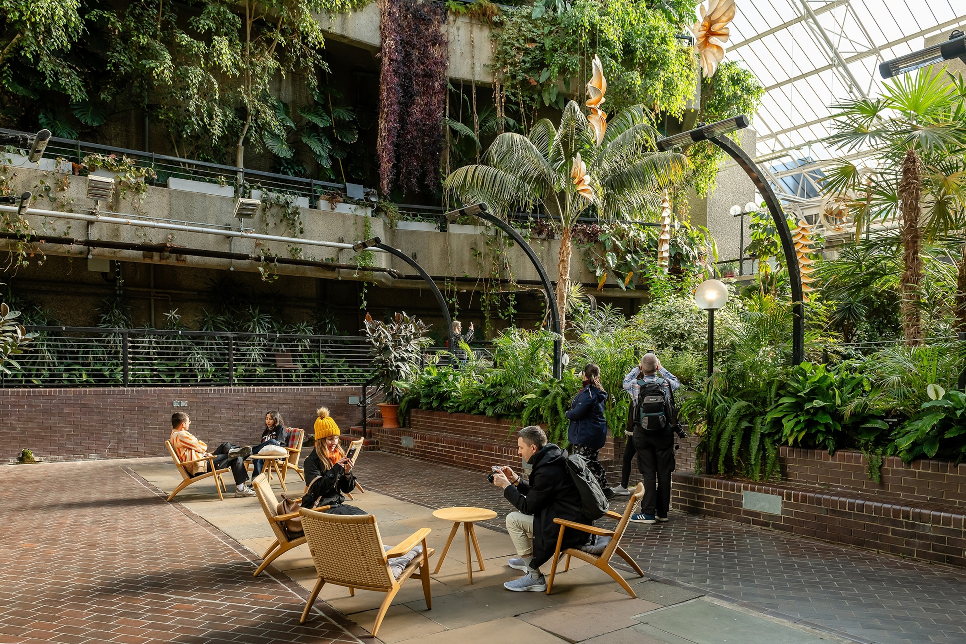 People lounge in chairs at the Barbican Centre Conservatory surrounded by plants.
