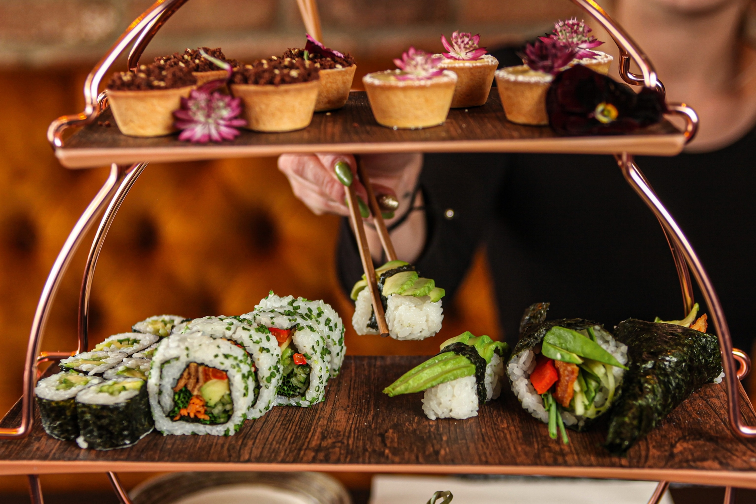 Afternoon tea platter with sushi rolls and cakes on a tiered platform