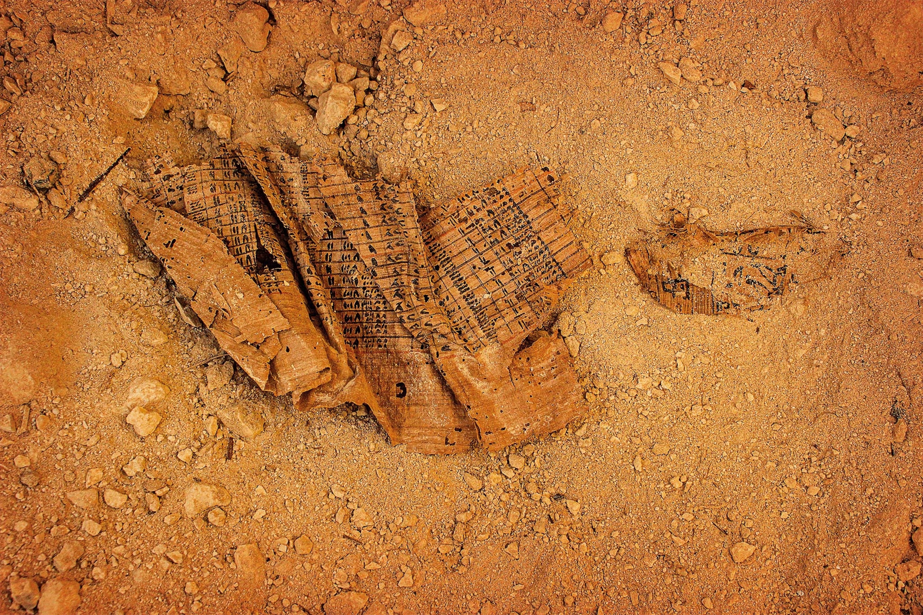 Papyri with writing sits crumpled on orange sand