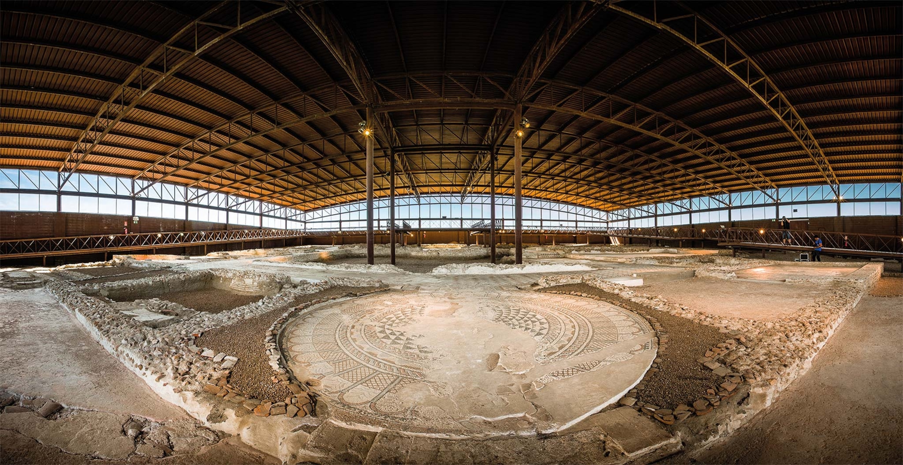 A roof now protects the fourth-century Villa of Maternus at Carranque. In the foreground is the portico, whose circular mosaic once welcomed guests. The roof’s four supporting pillars rest in what would have been the central garden.