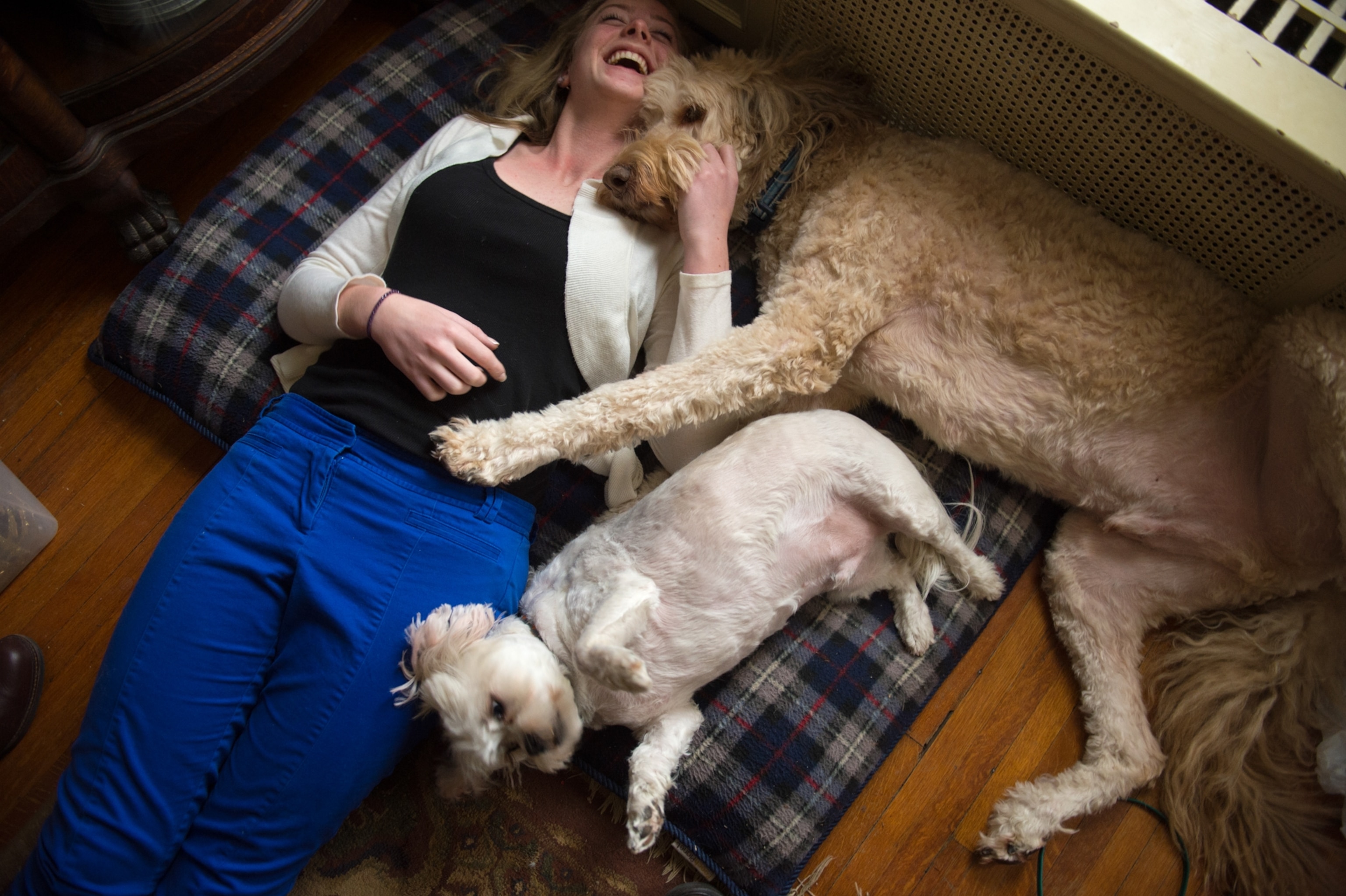 A young woman laying back and smiling as she cuddles with her two dogs.