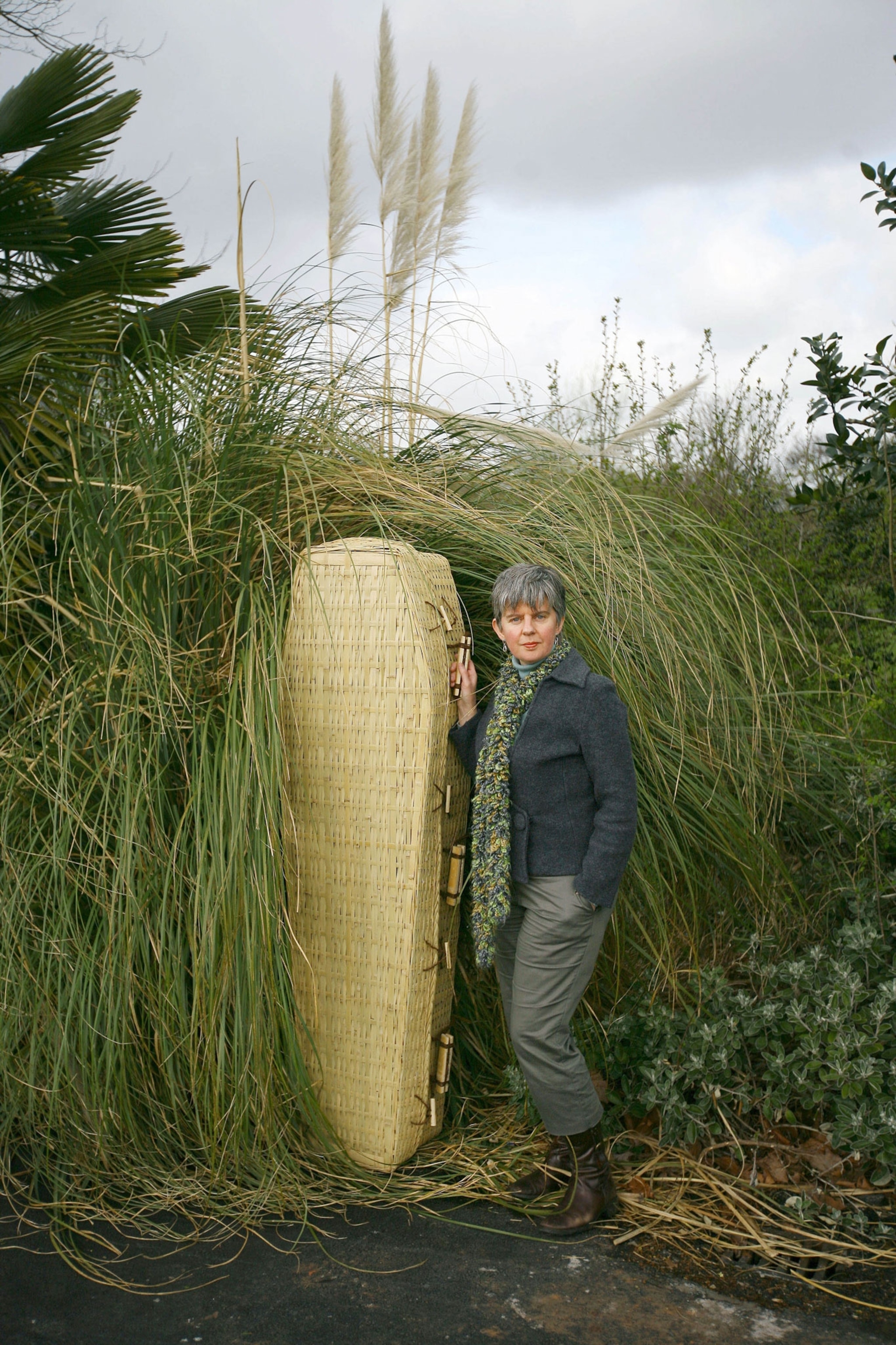 a woman stands next to a bamboo coffin in a park