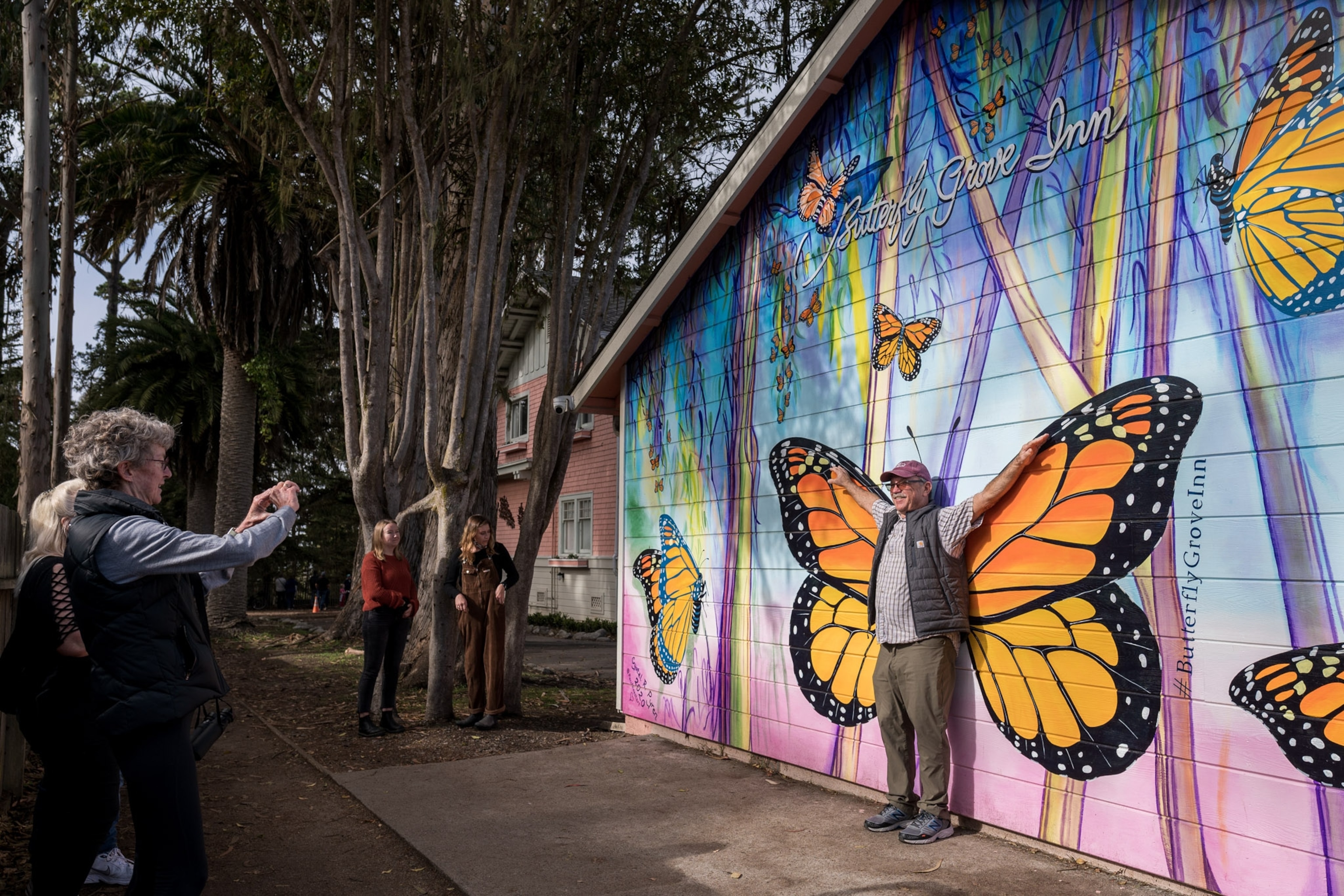 A man is photographed with his arms extended in front of a monarch butterfly mural.