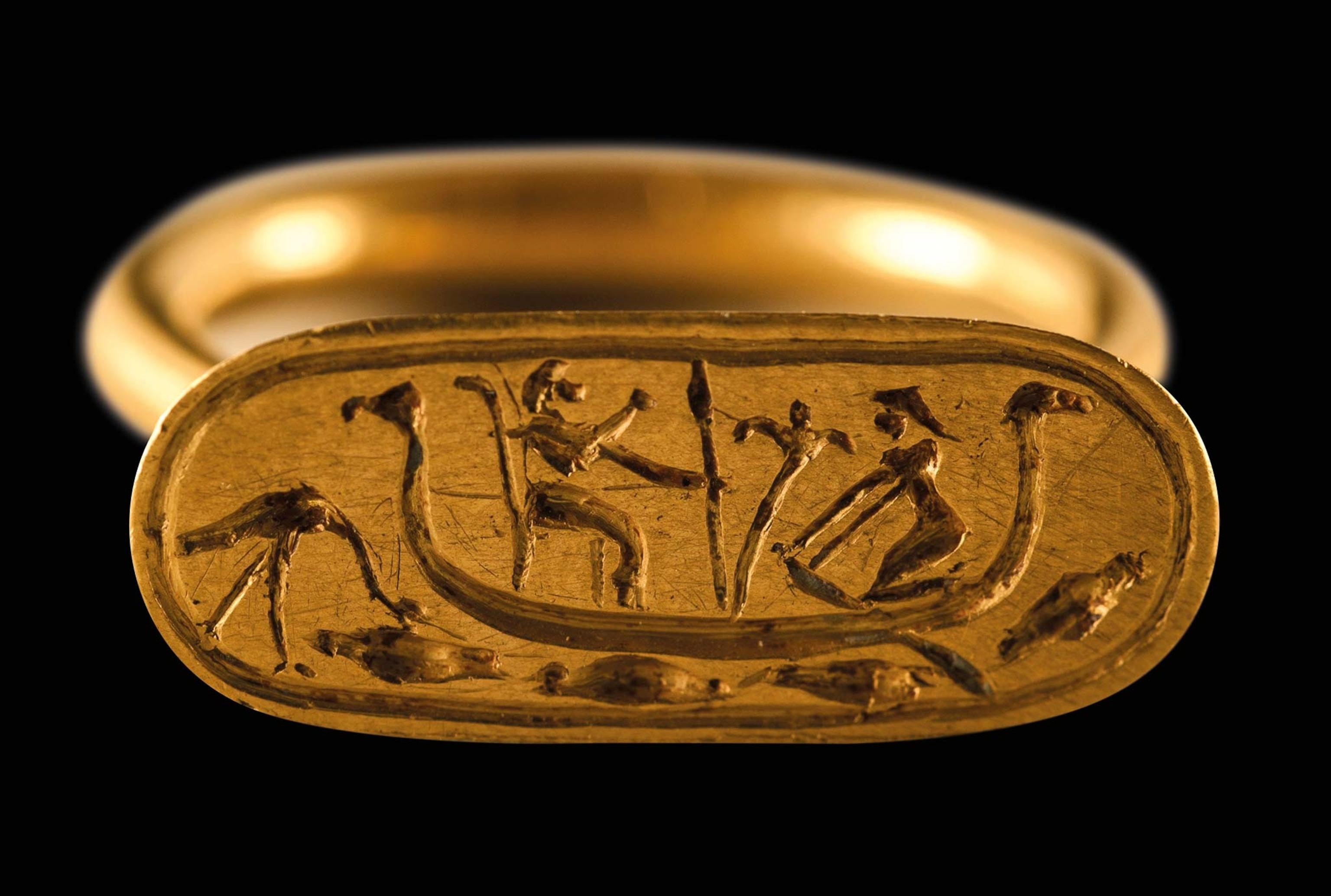stylized Nile scene is engraved on a gold ring’s flat surface, showing a boat with an oarsman and a seated figure with the head of a canid
