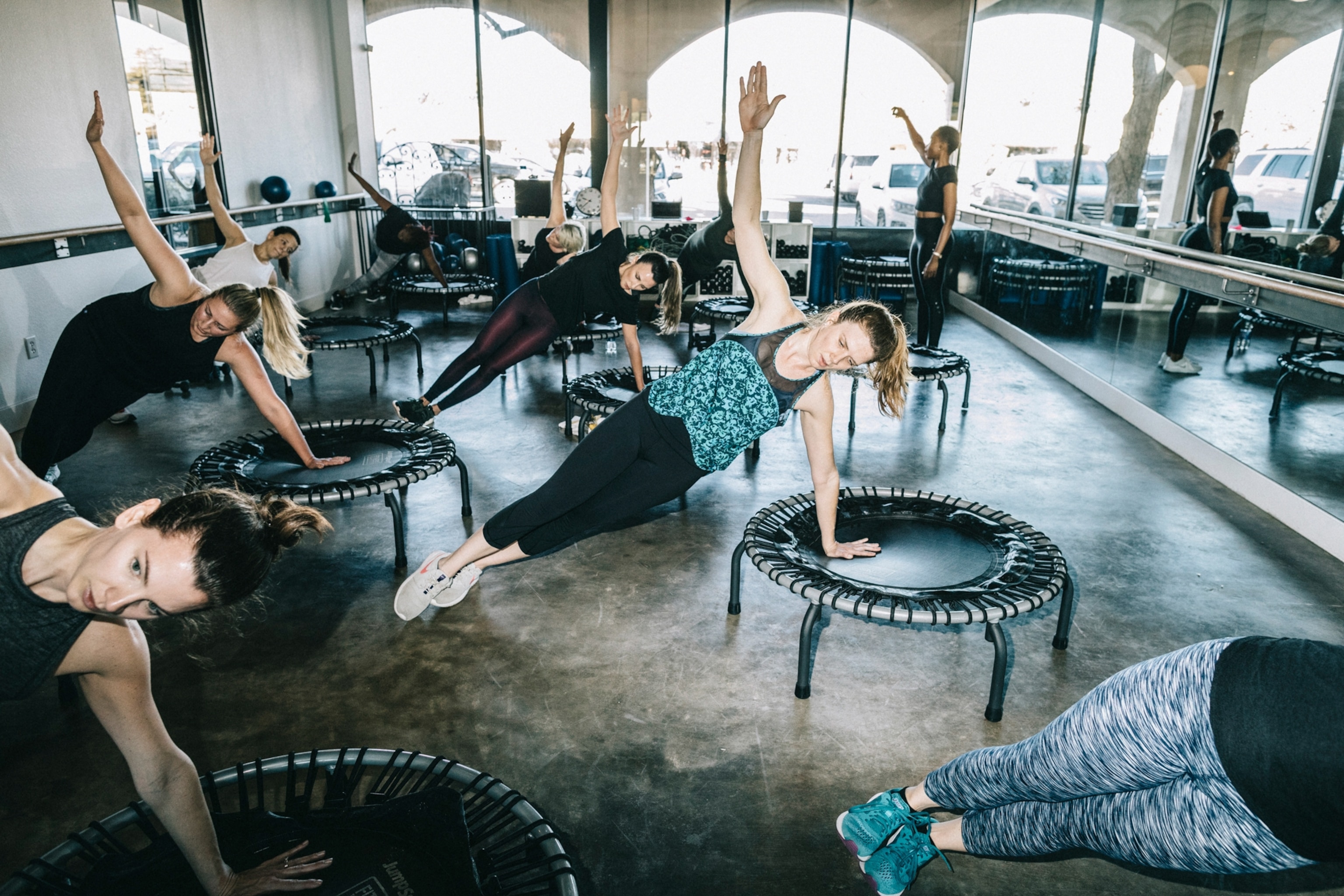 A class of women all using one arm to support their weight as they lean on small trampolines
