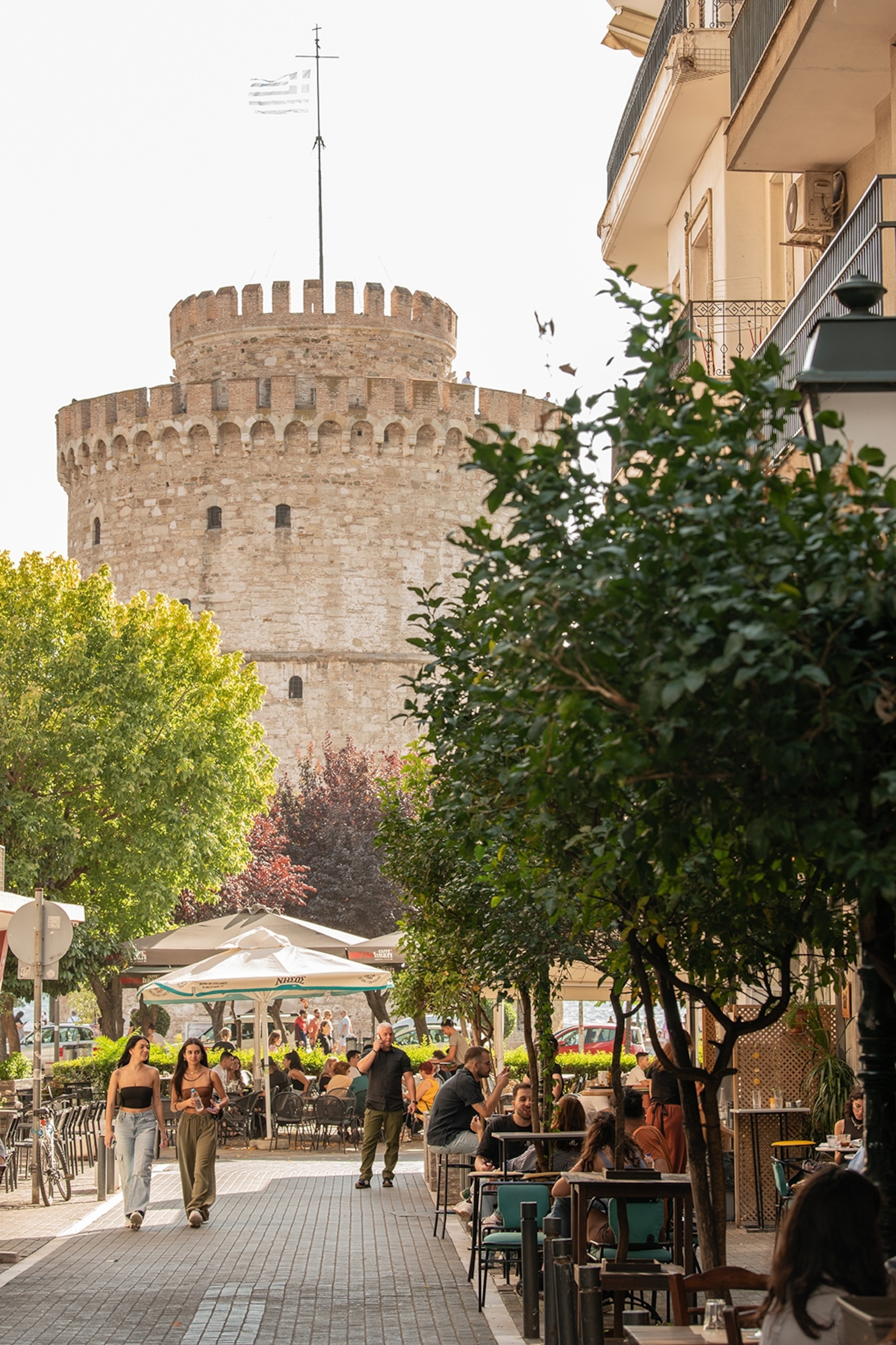 An wide, low stone tower with a busy, tree-lined street promenade in front.