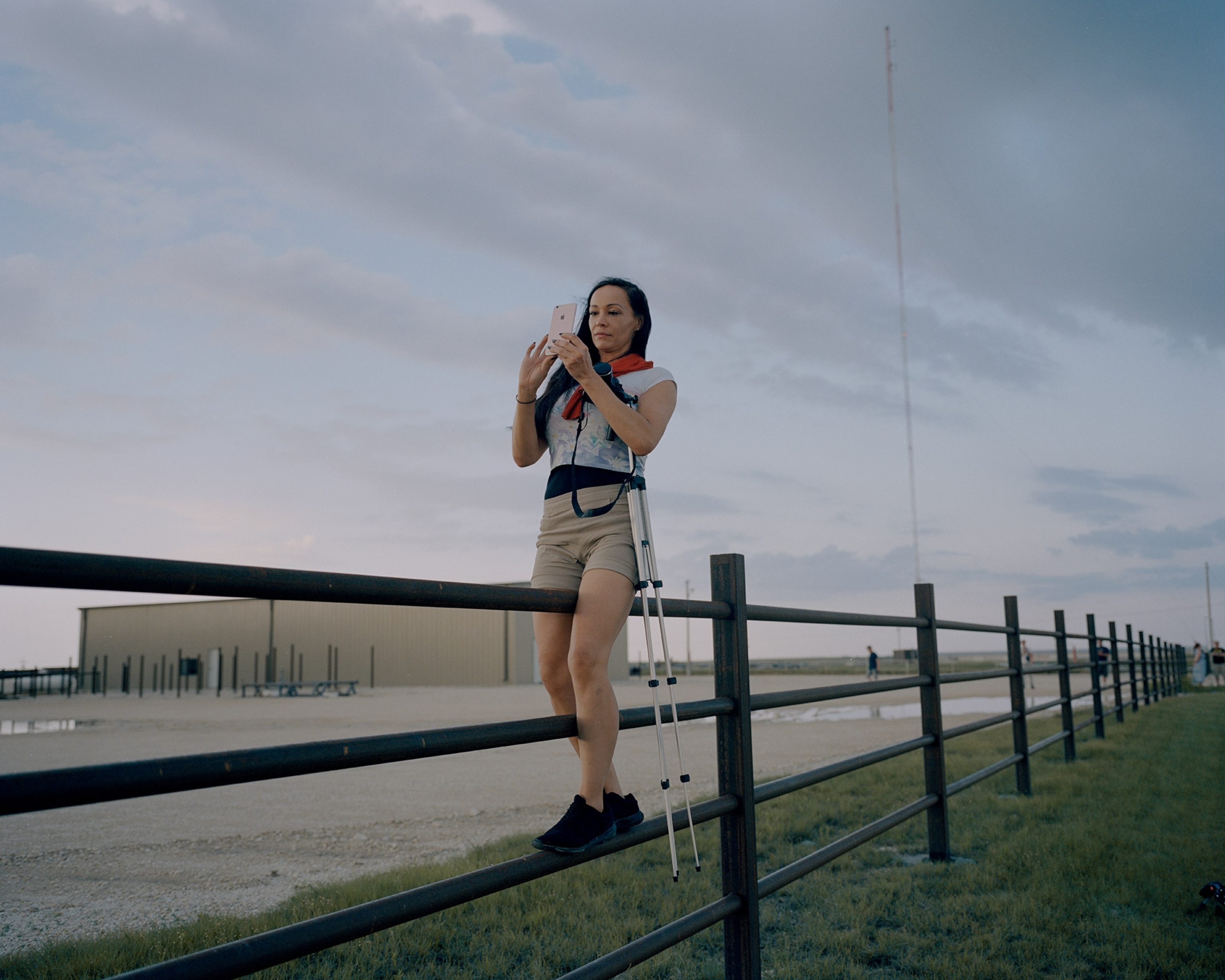 A storm chaser balances on a fence as she photographs a storm