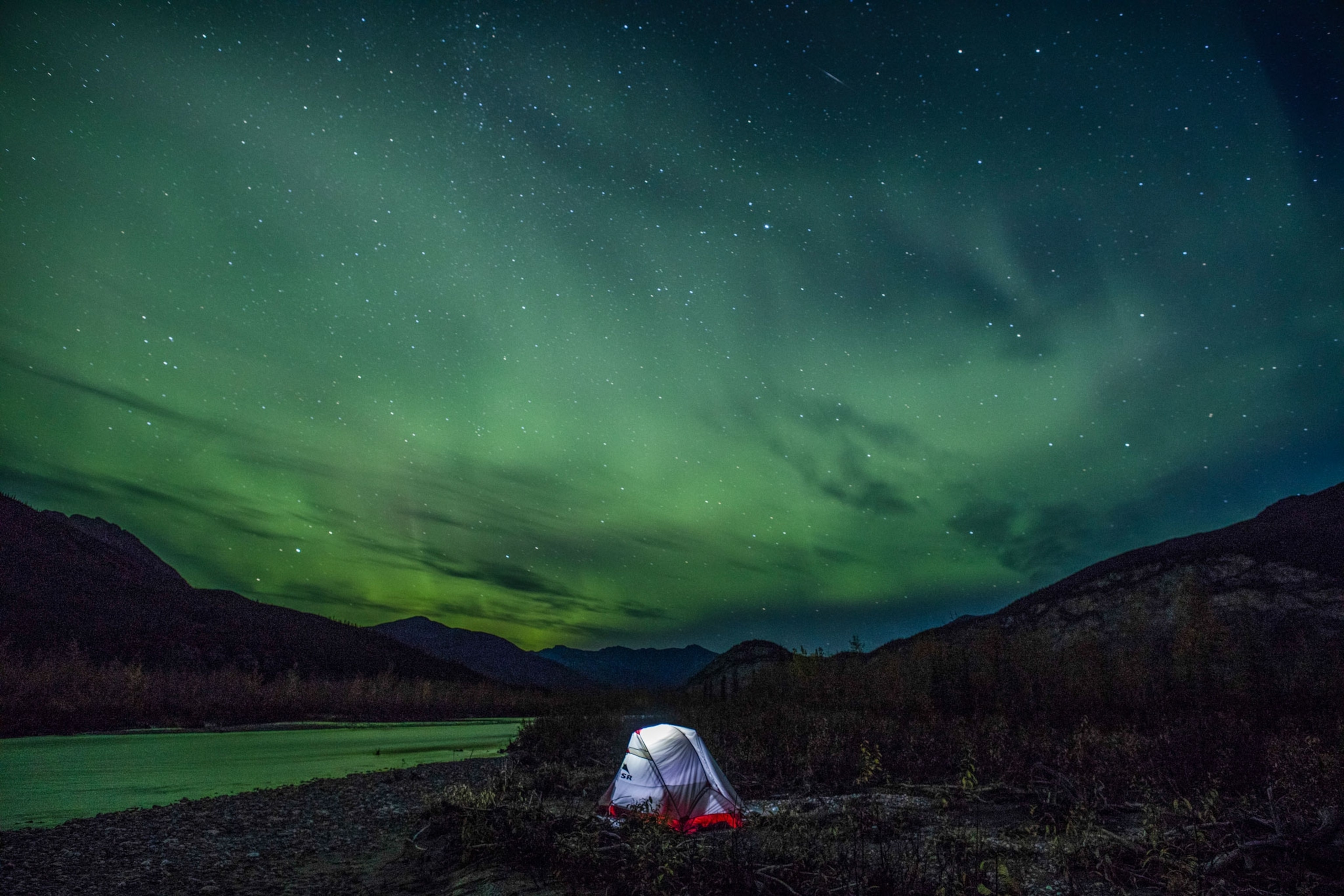 a white tent glowing from a internal light source under a sky illuminated green from northern lights