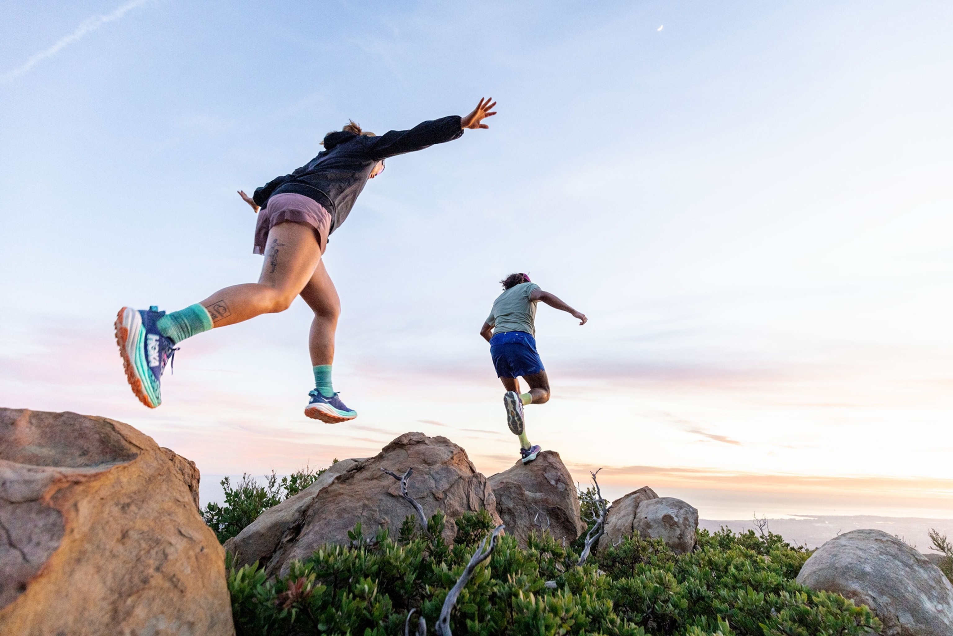 A man and woman leap across rocks.