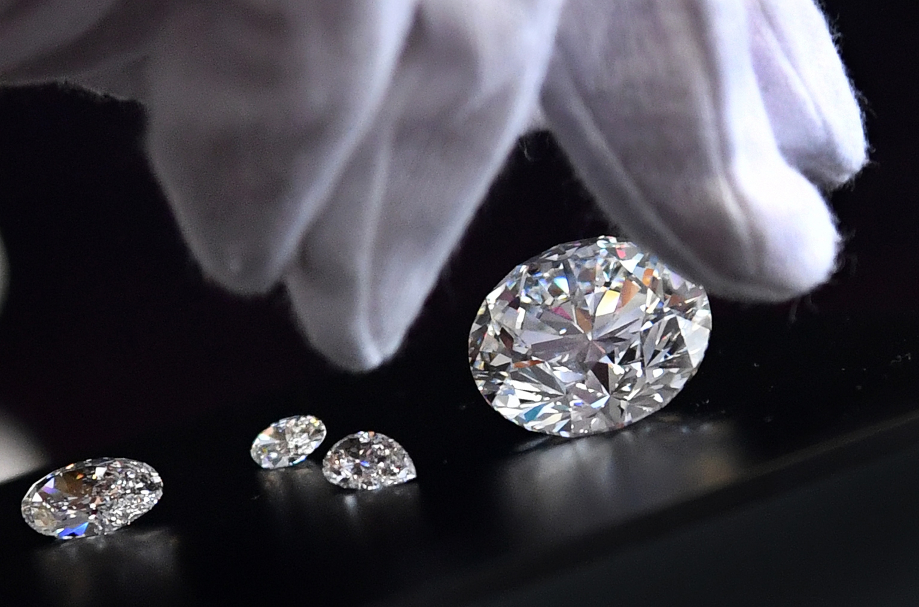 A white gloved hand reaches for a polished round-cut diamond.