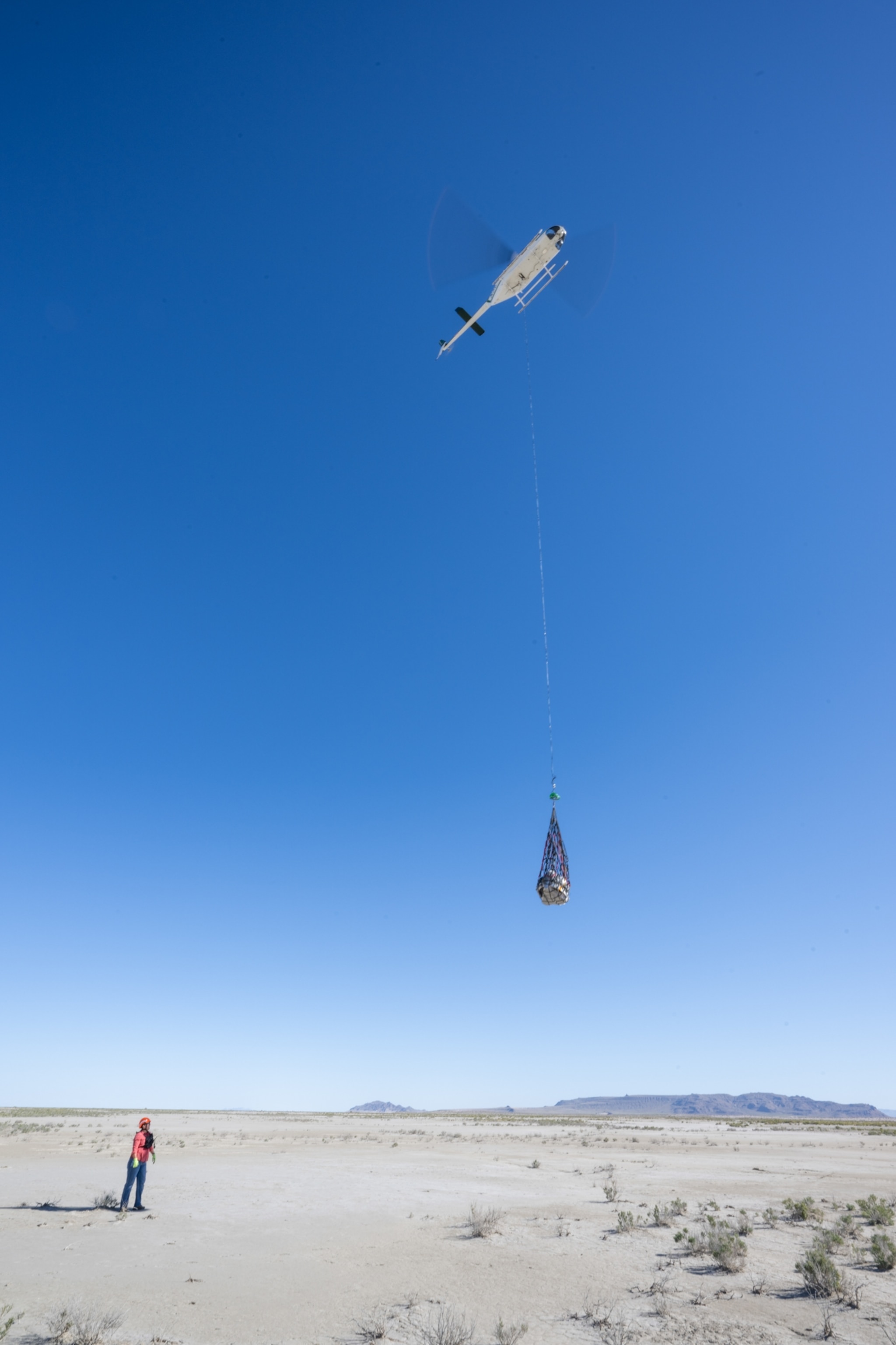 A recovery team member watches from below as a helicopter carries off a dummy capsule during a training mission.