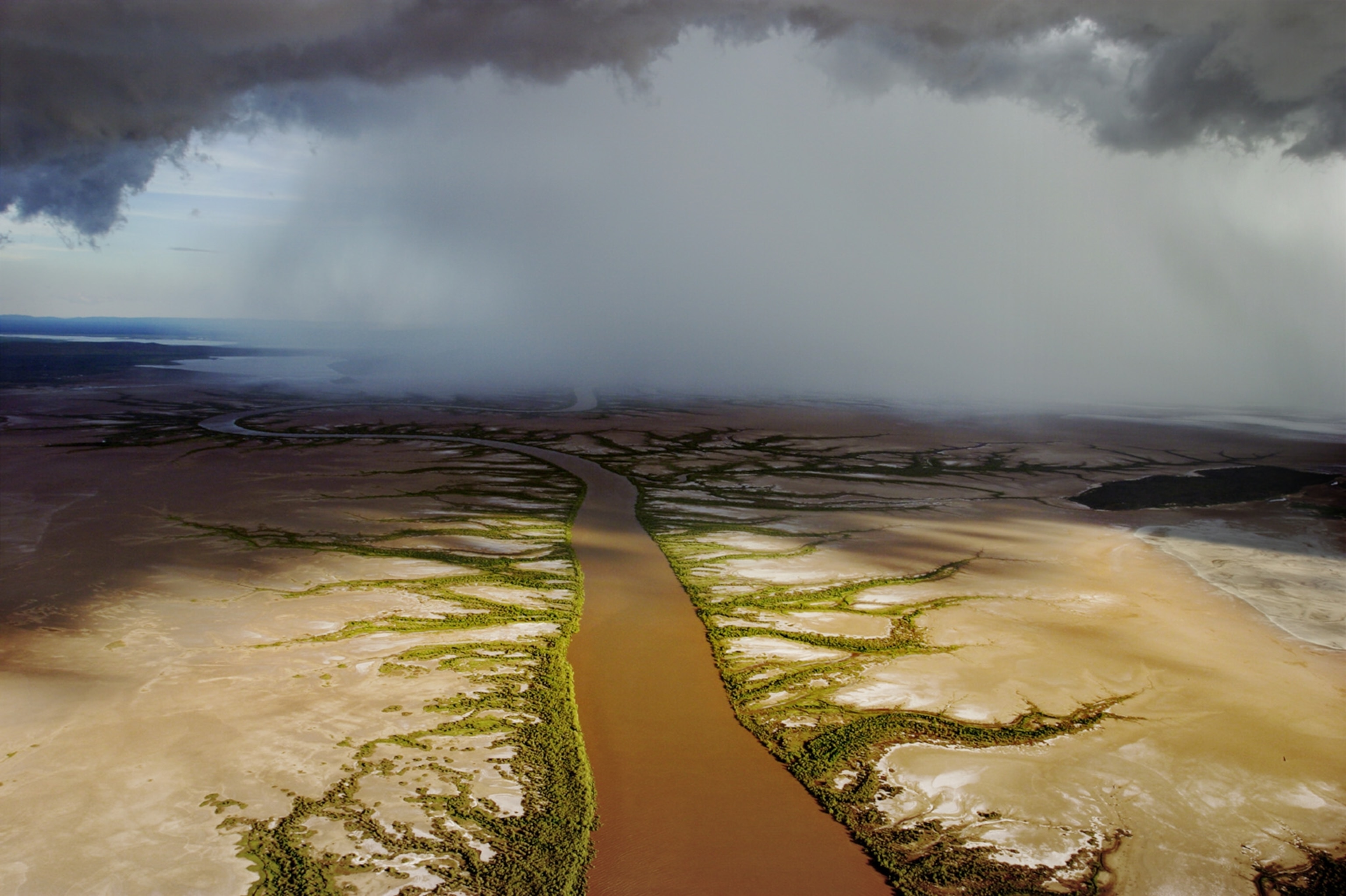 An aerial view of a coffee-colored river with rain in distance