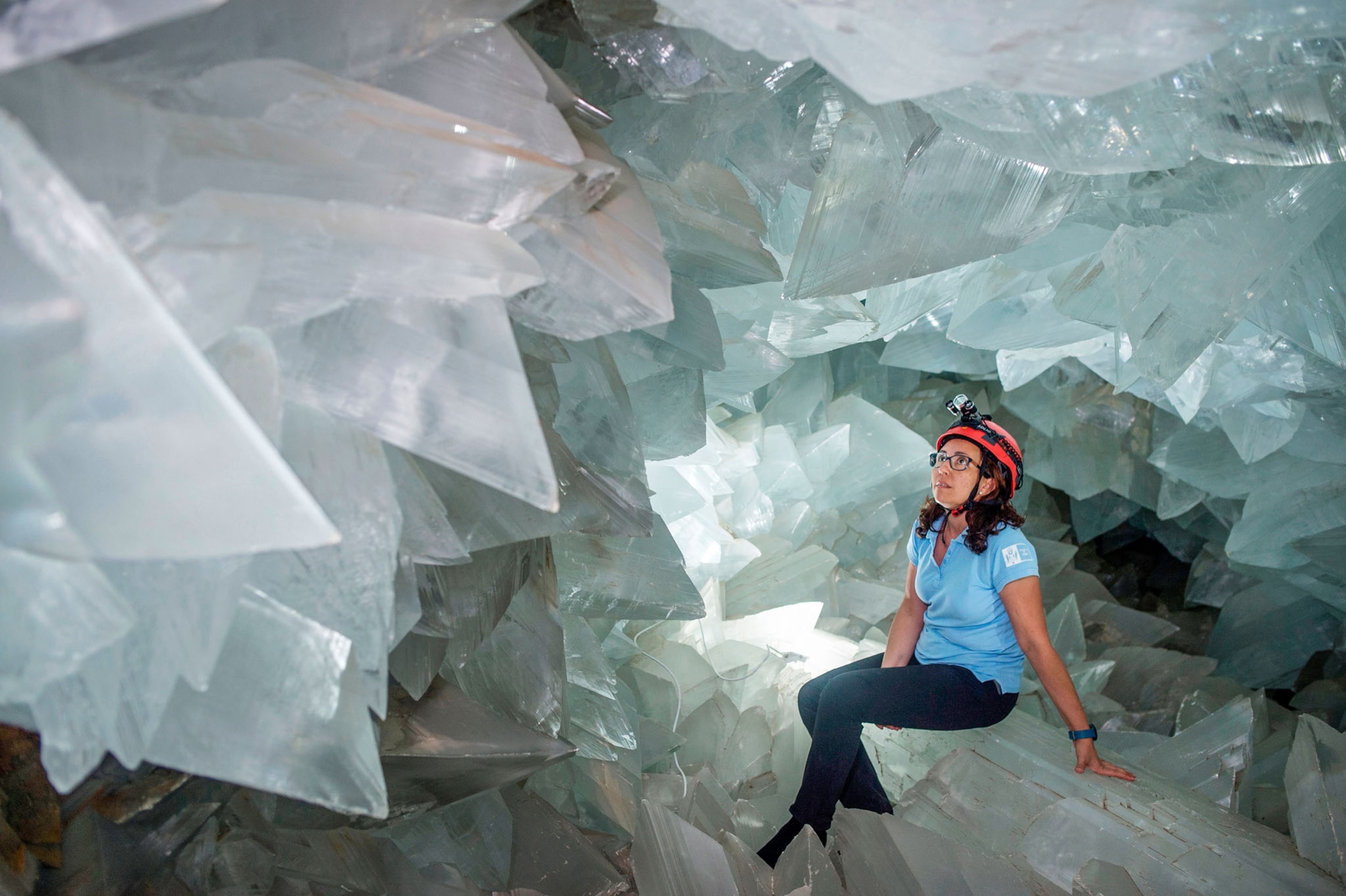 a woman sitting on large crystal surrounded by crystals.