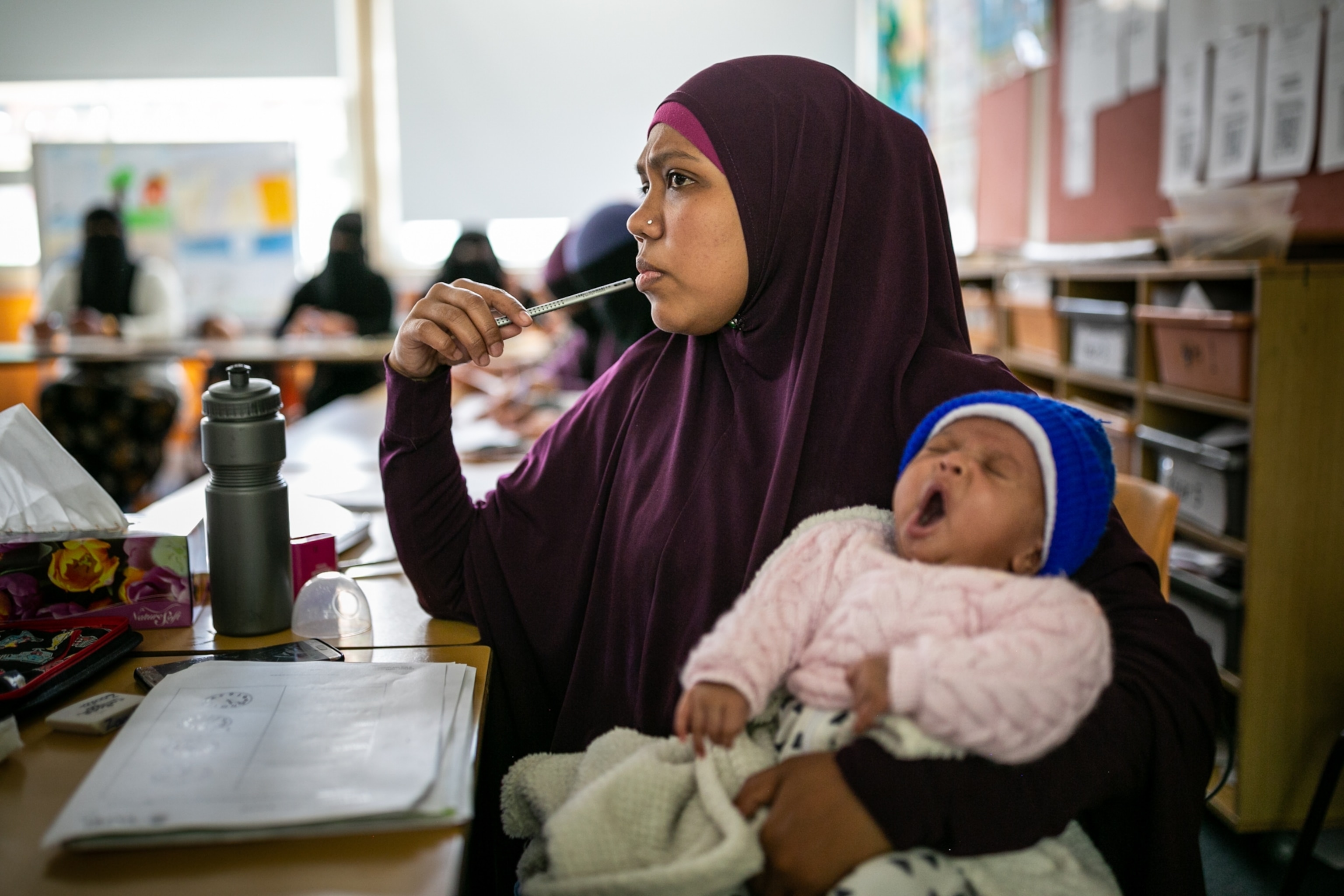 a woman sitting at a desk with a pencil to her lip, holding a child