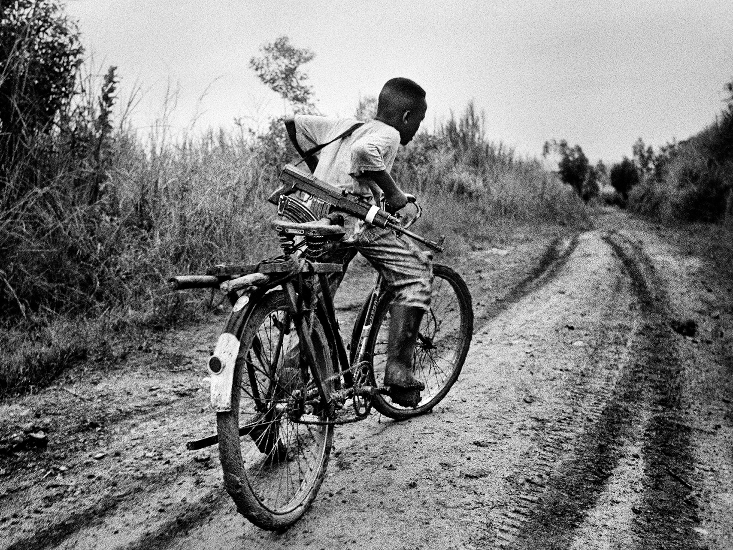 a boy with an assault rifle biking to base camp