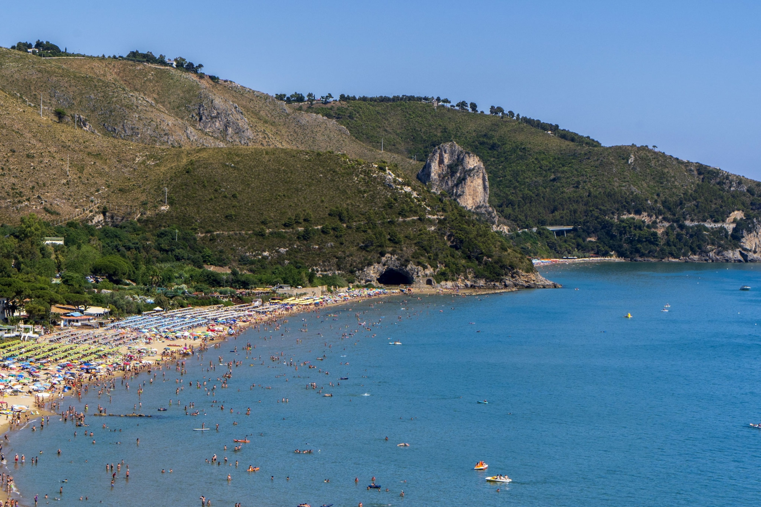 a view of umbrellas and beachgoers near the ocean at the base of a mountain