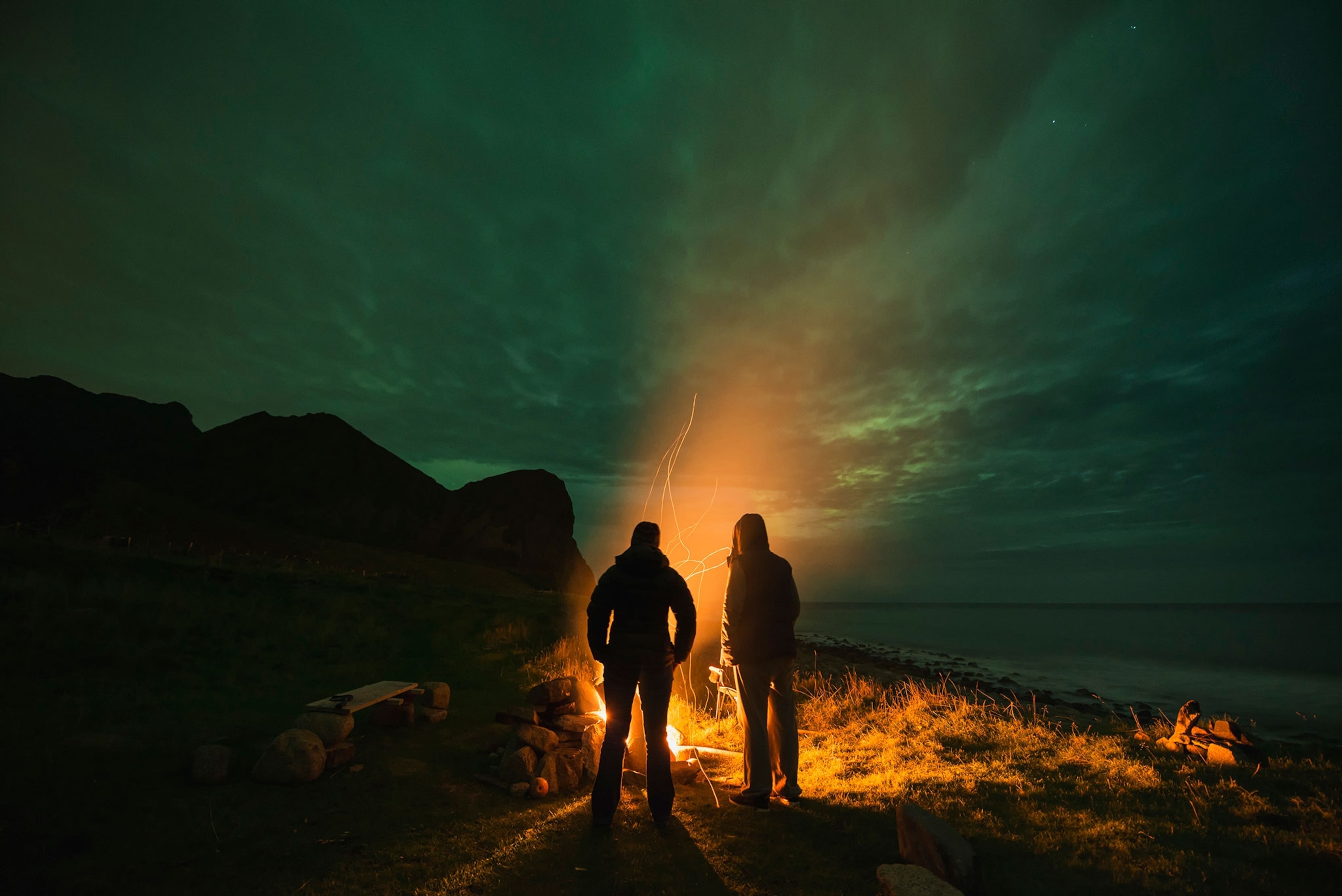 two people standing by a campfire in Norway under the aurora borealis