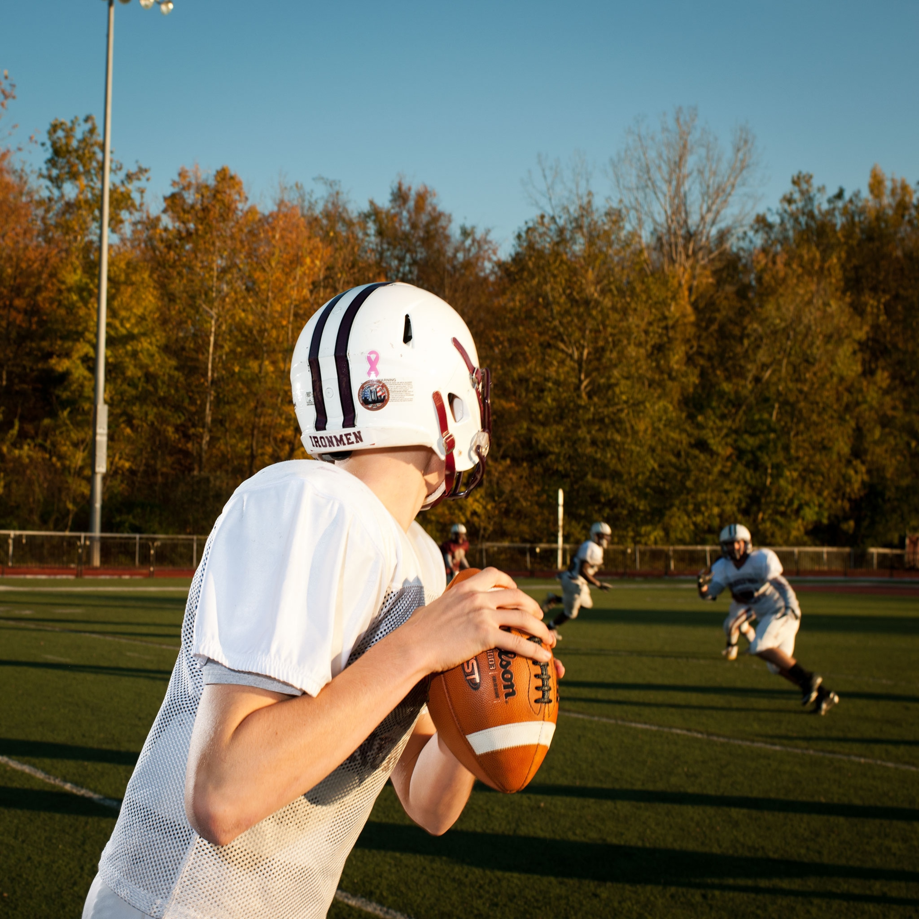 A young boy quarter back in a white and red uniform about to throw a football to a teammate.