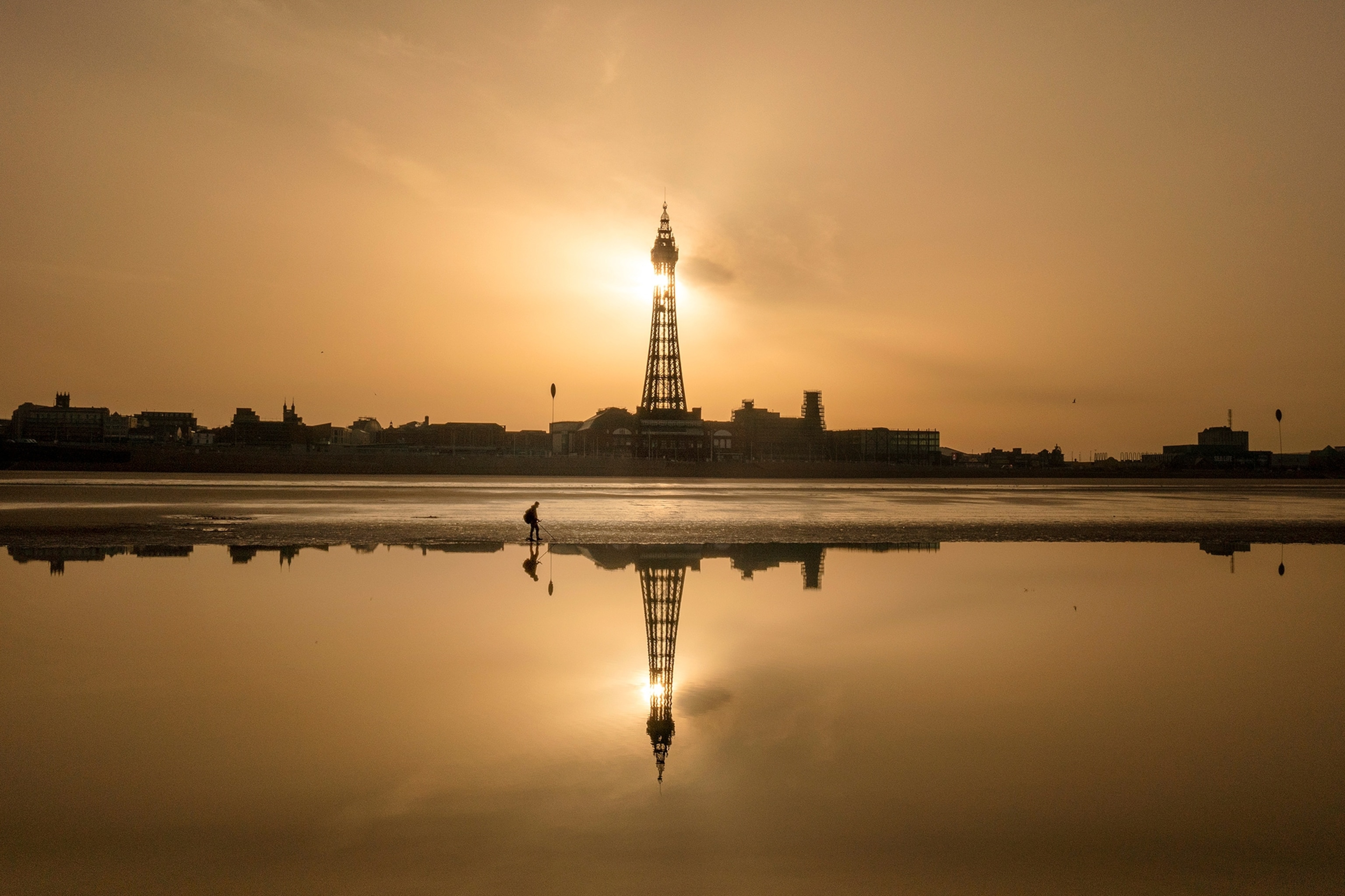 n an aerial view from a drone, a metal detectorist searches the beach as the sun rises behind Blackpool Tower.