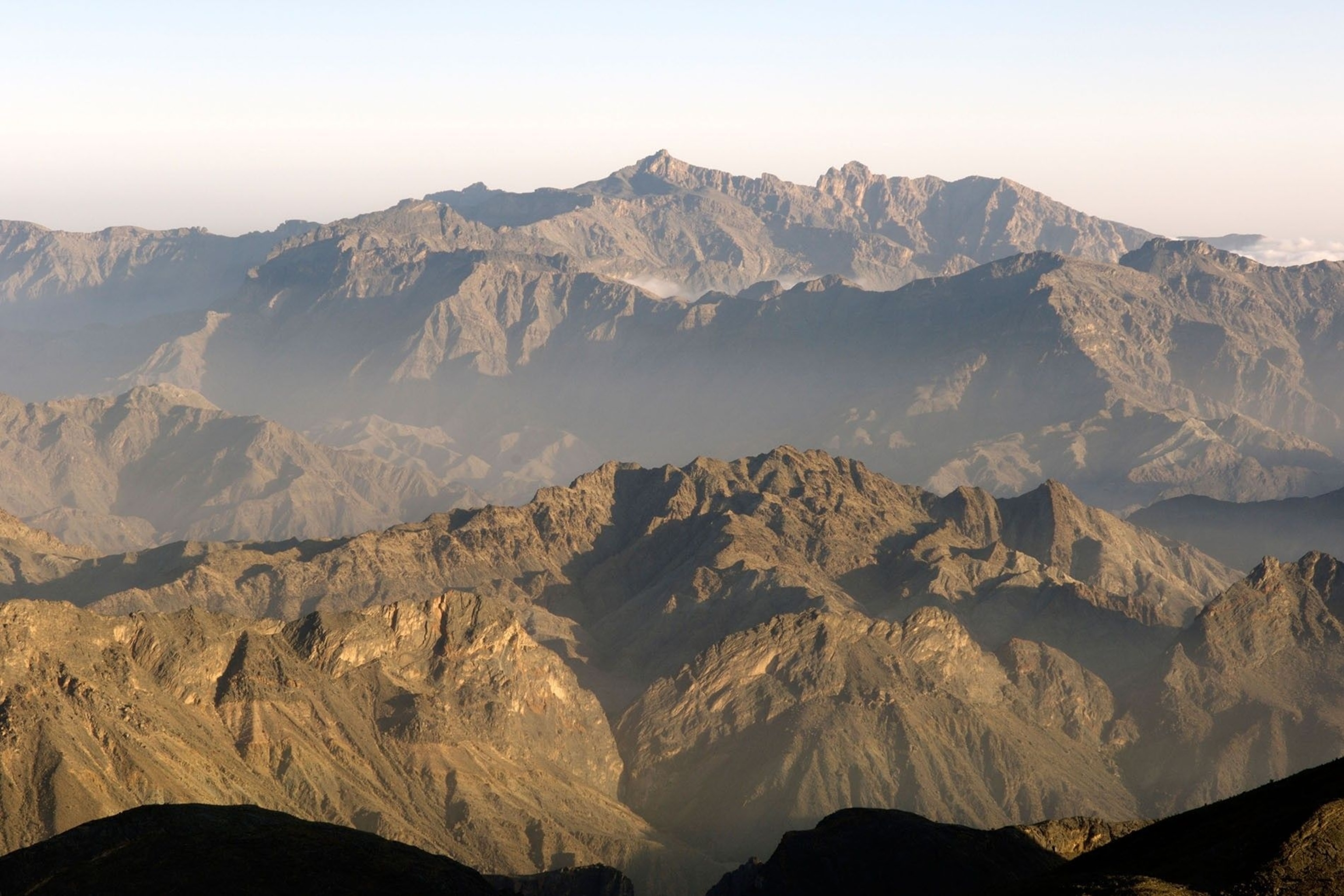 The peaks of the Hajar Mountains’ western range stretch off into a sand-coloured sky.