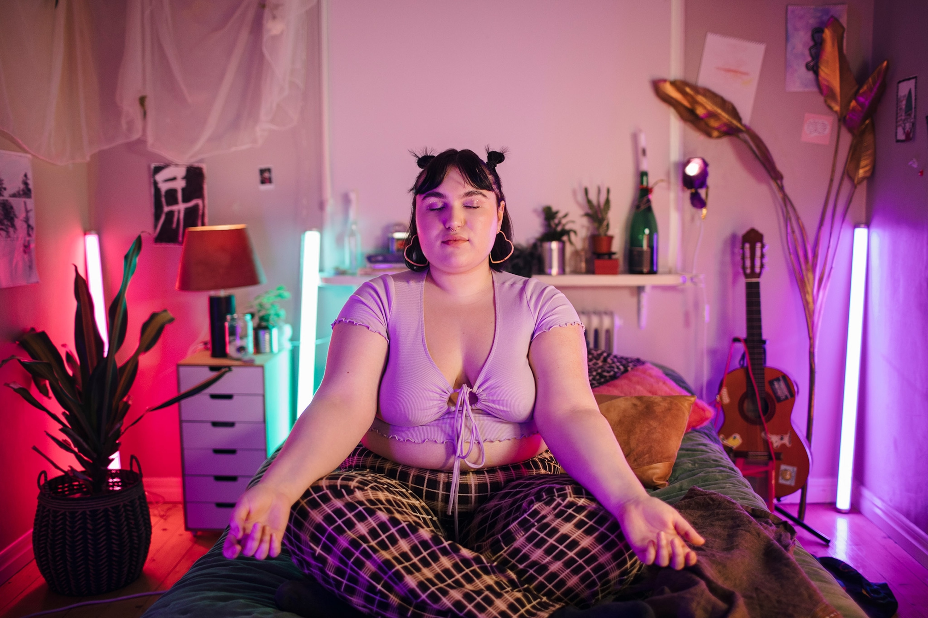 Young woman meditating on bed in illuminated bedroom at home