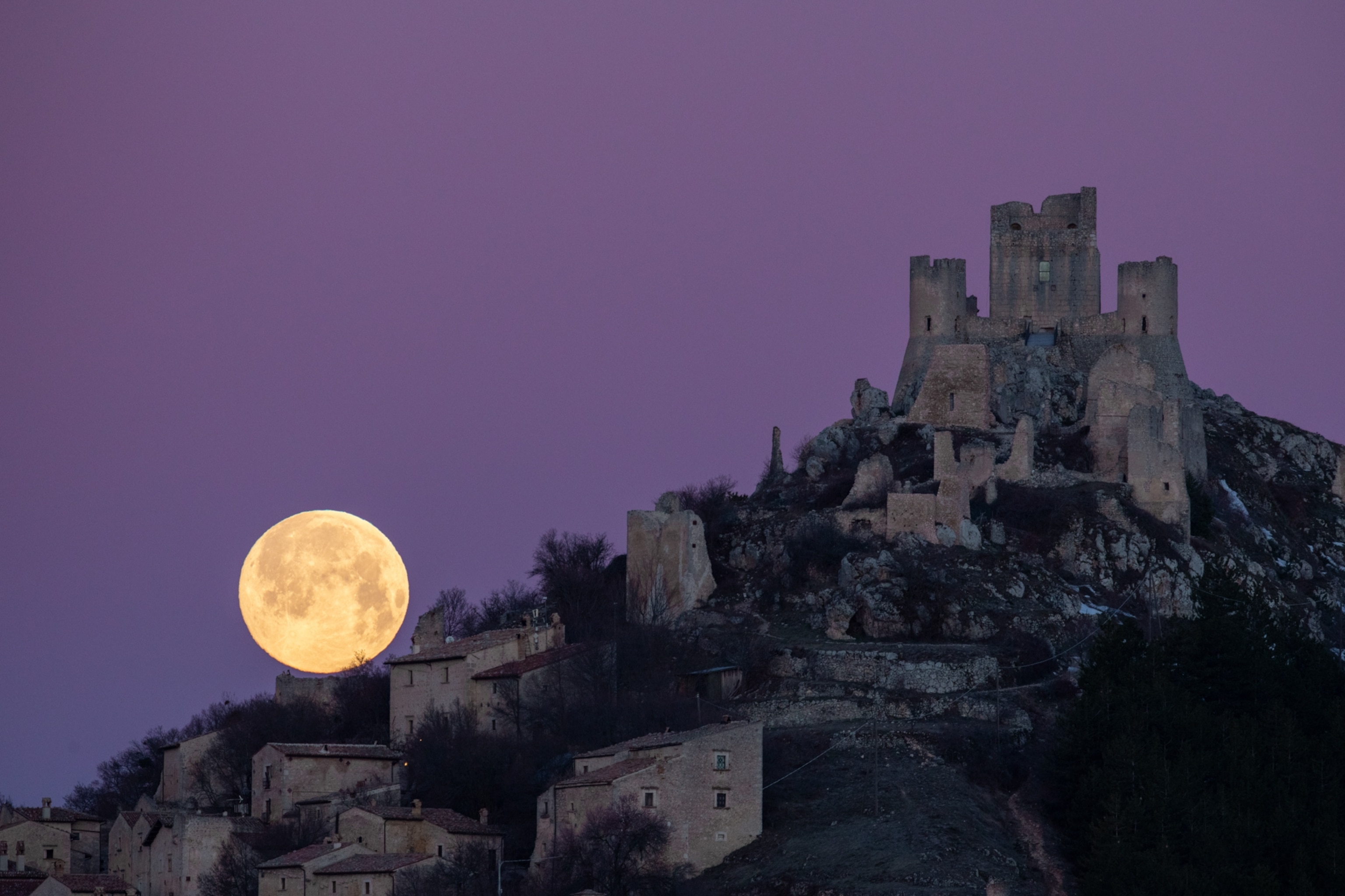 A full moon sets behind Rocca Calascio castle in Italy.
