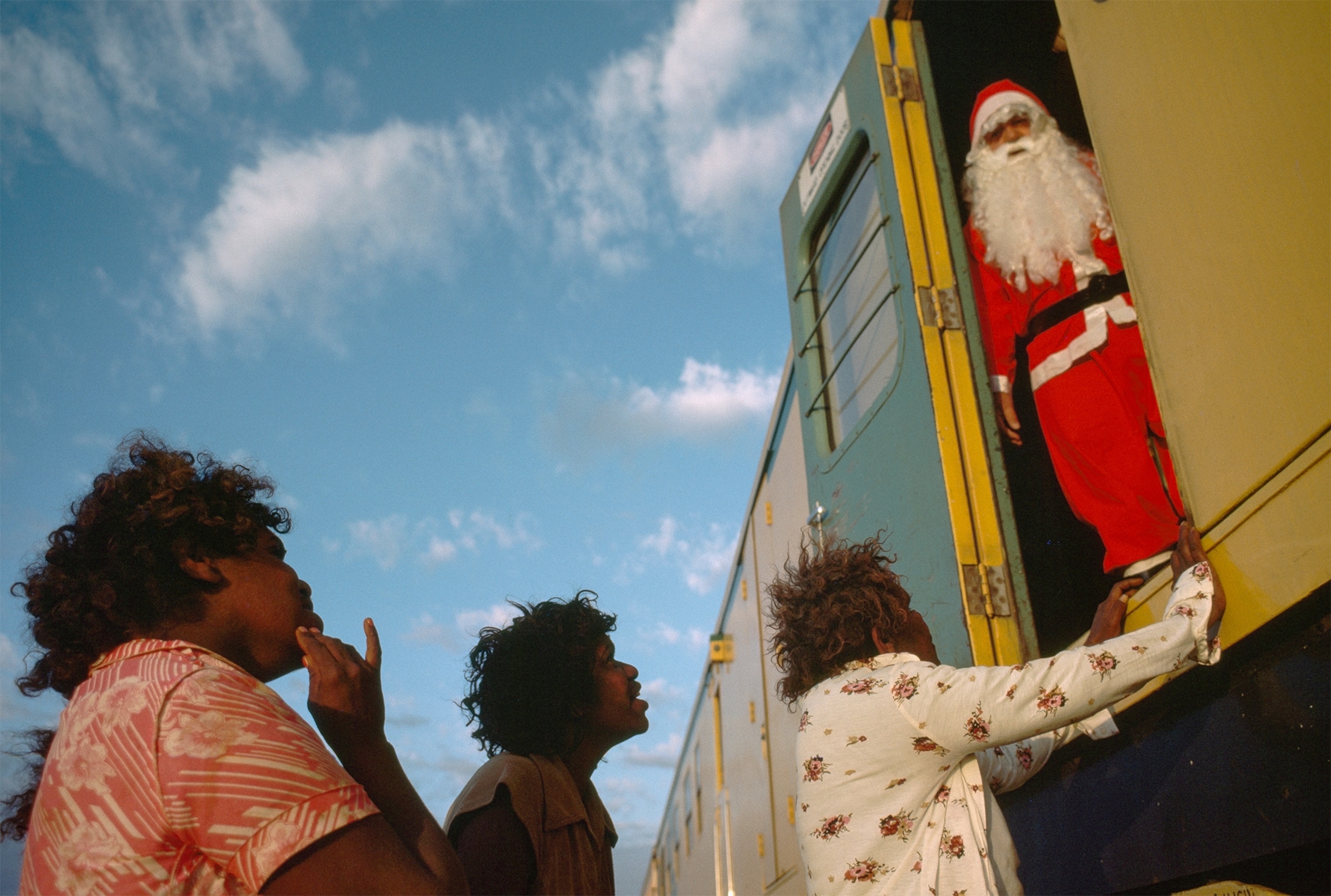 a man dressed as Santa Claus greeting Aborigines from a supply train in Australia.