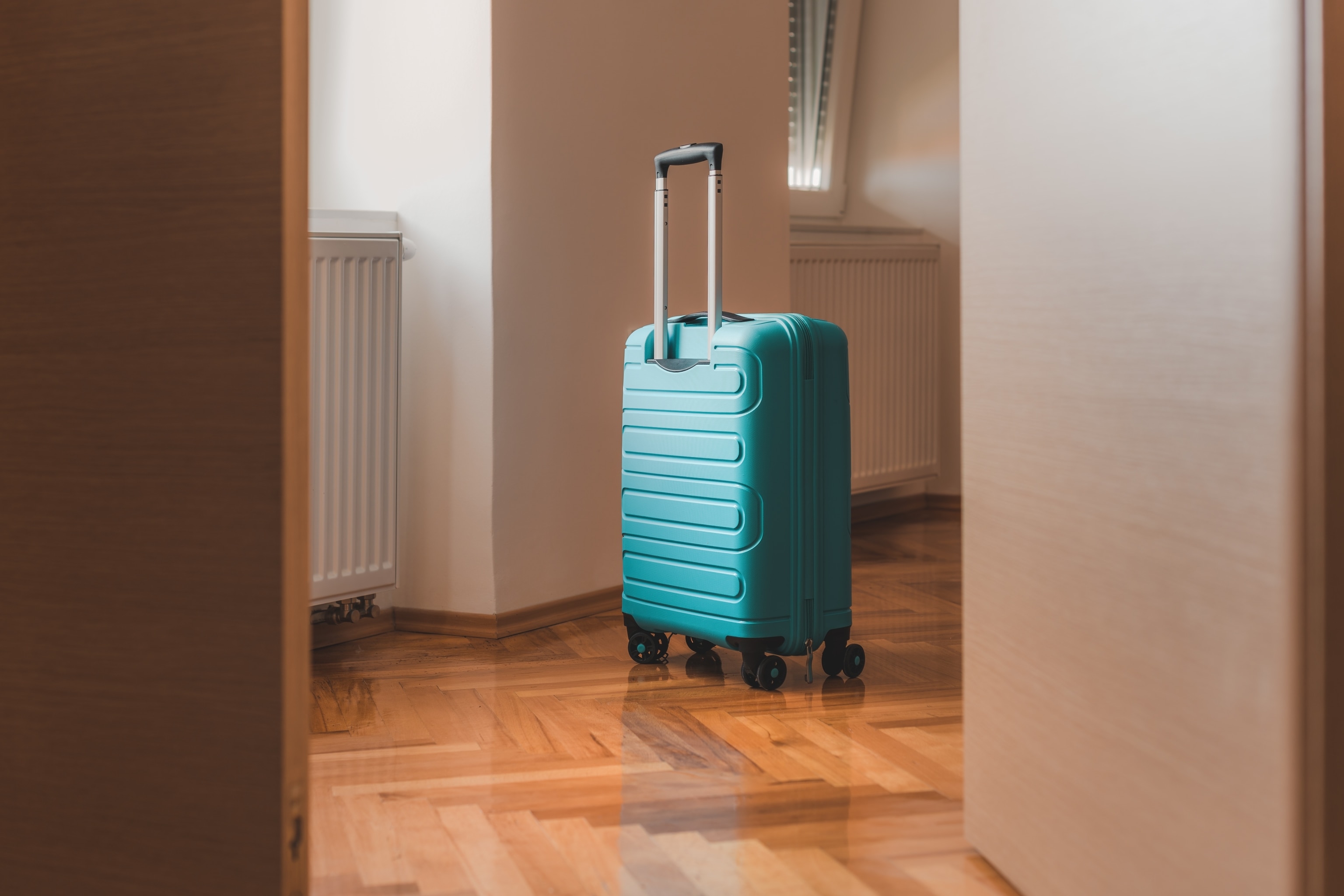 Turquoise blue rollaboard suitcase sitting in empty room between doorway.