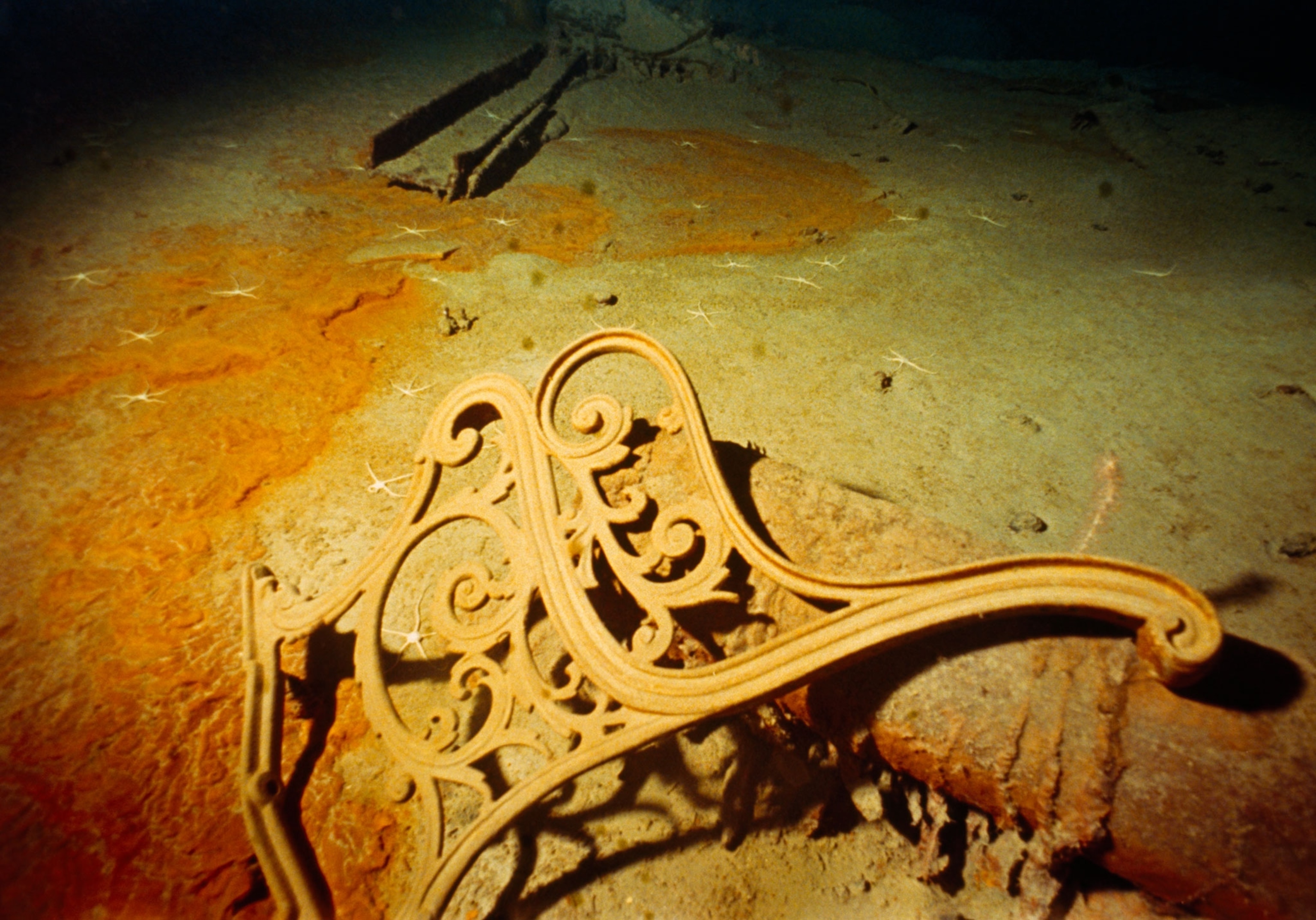 The side of a metal bench laying on another piece from the wreckage of the Titanic on the ocean floor.