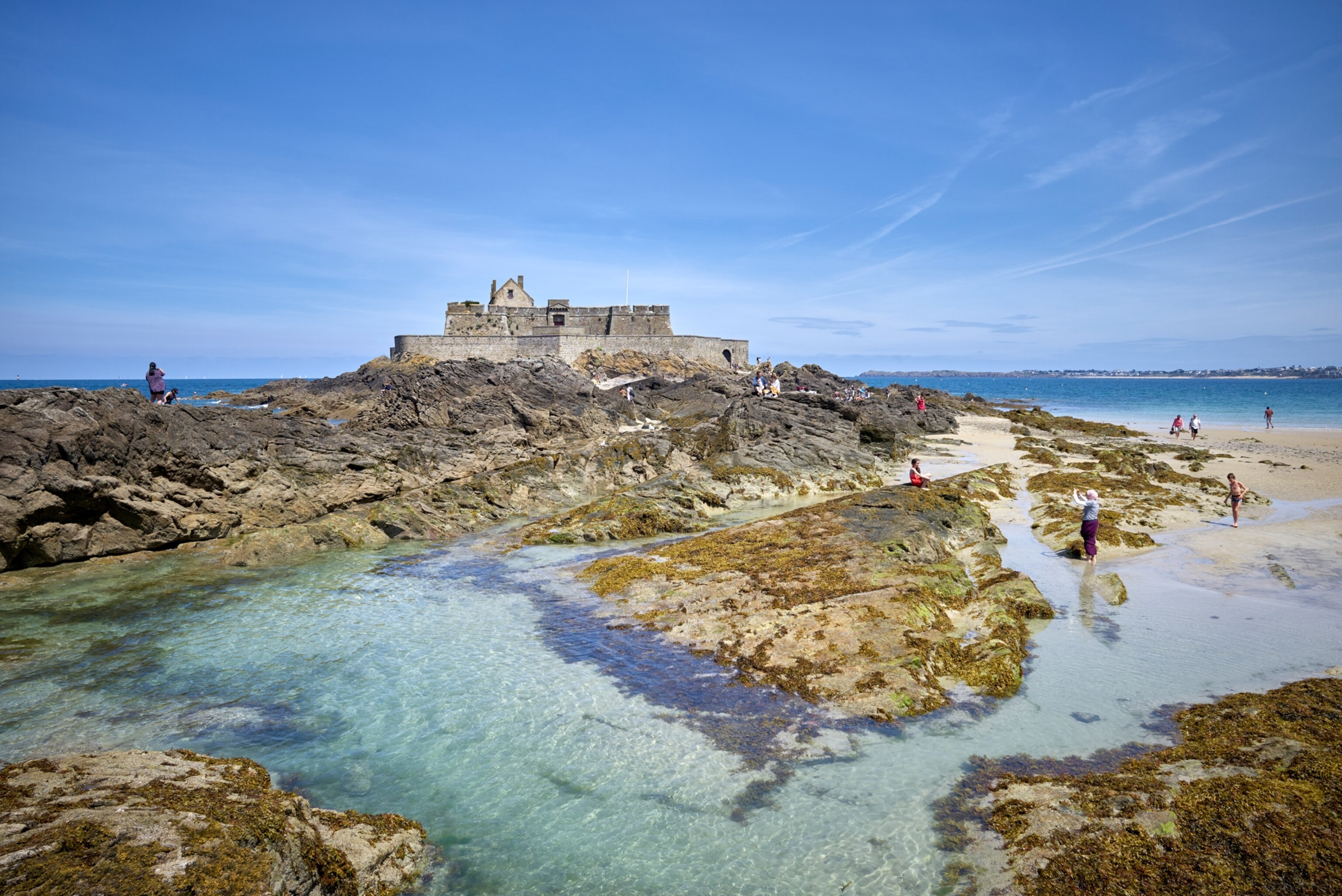 Tourists exploring the National Fort of St. Malo and the surrounding pools formed at low tide.