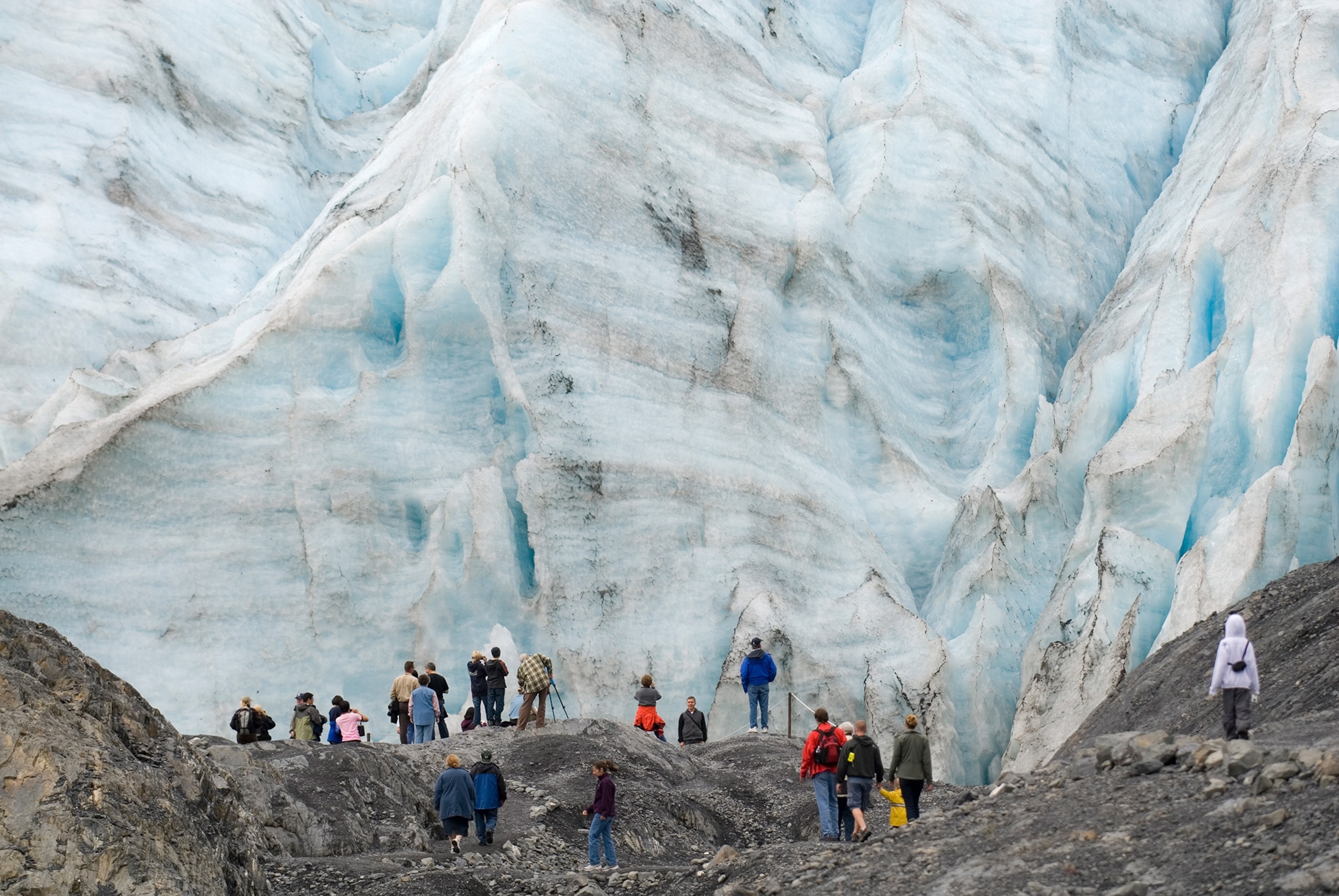 A glacier wall fills the frame as people stand below.