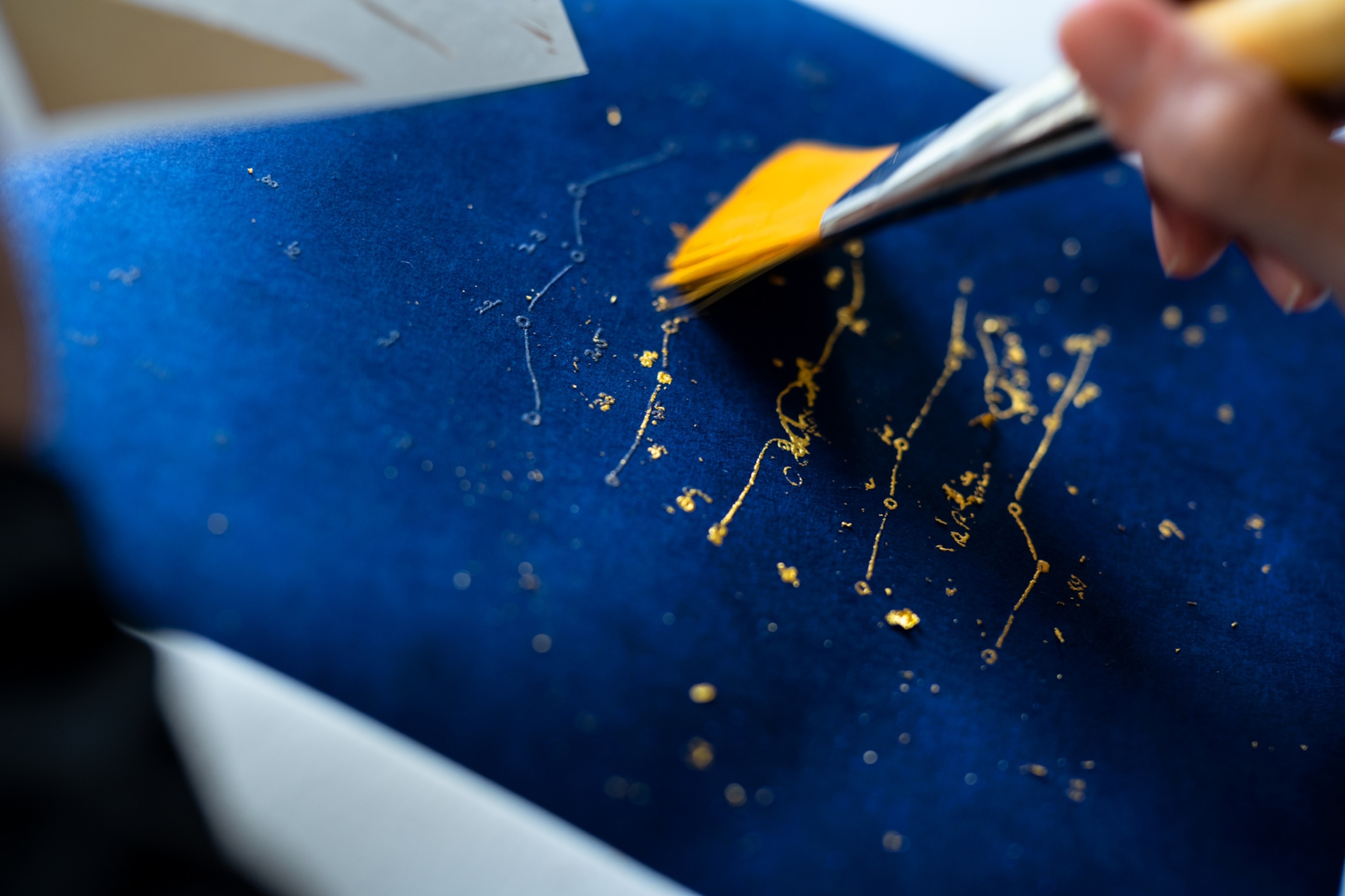 Picture of hand brushing blue plate with gold dust.