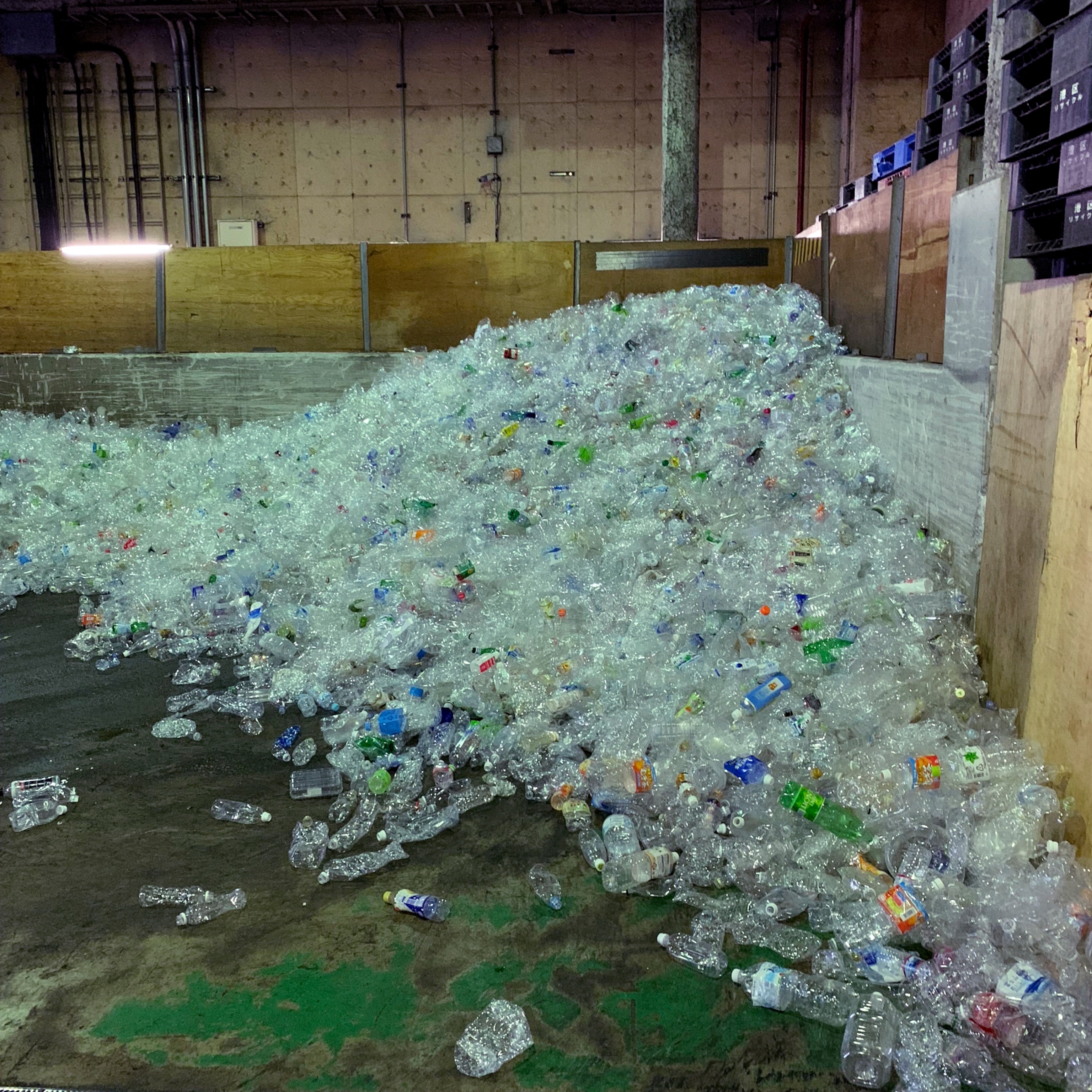 a pile of plastic bottles, most clear but some green and blue, in a recycling center