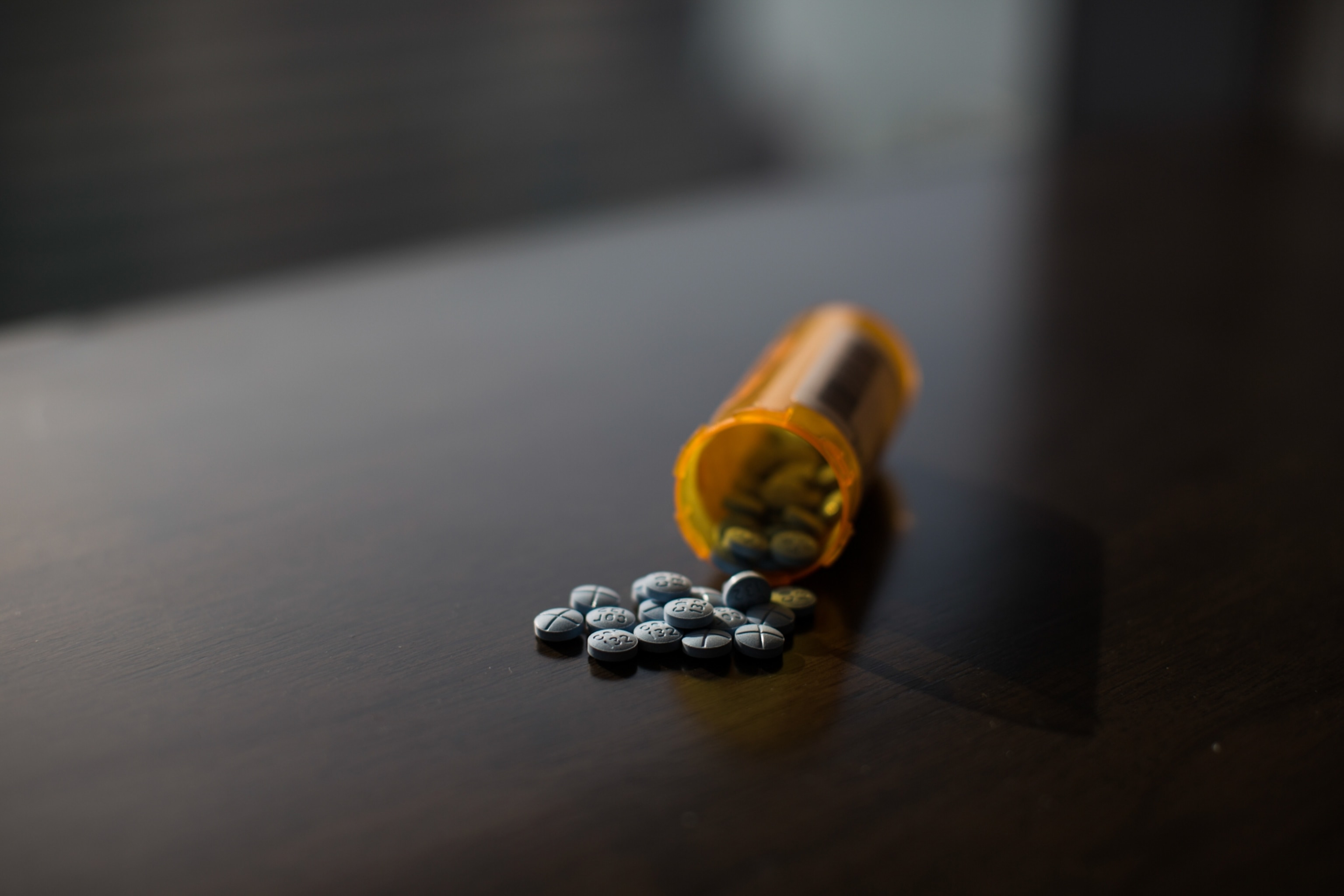 A pill container lies on its side with blue pills pouring out onto a tabletop.