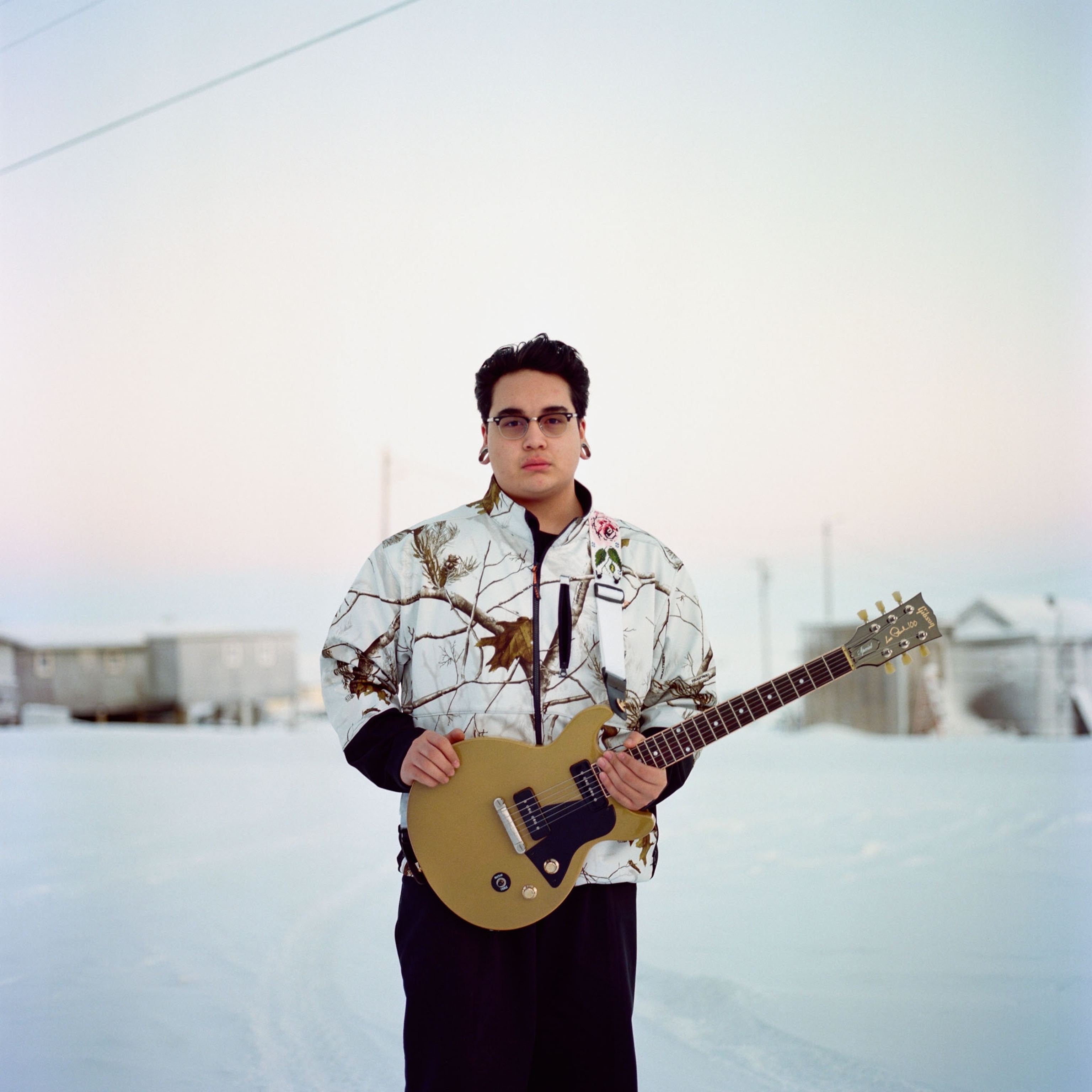 a young man posing for a portrait in the snow with a guitar