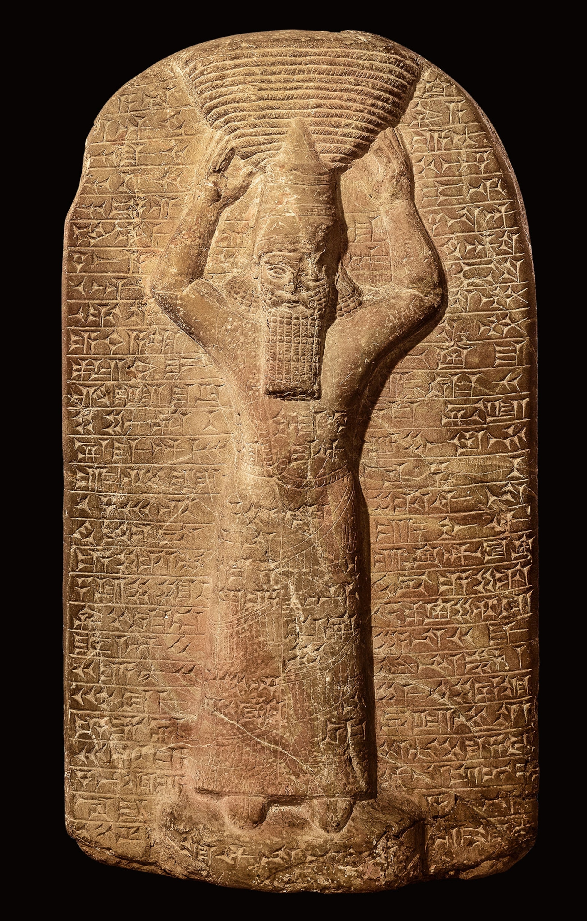 A marble stela depicts a king holding a basket on his head