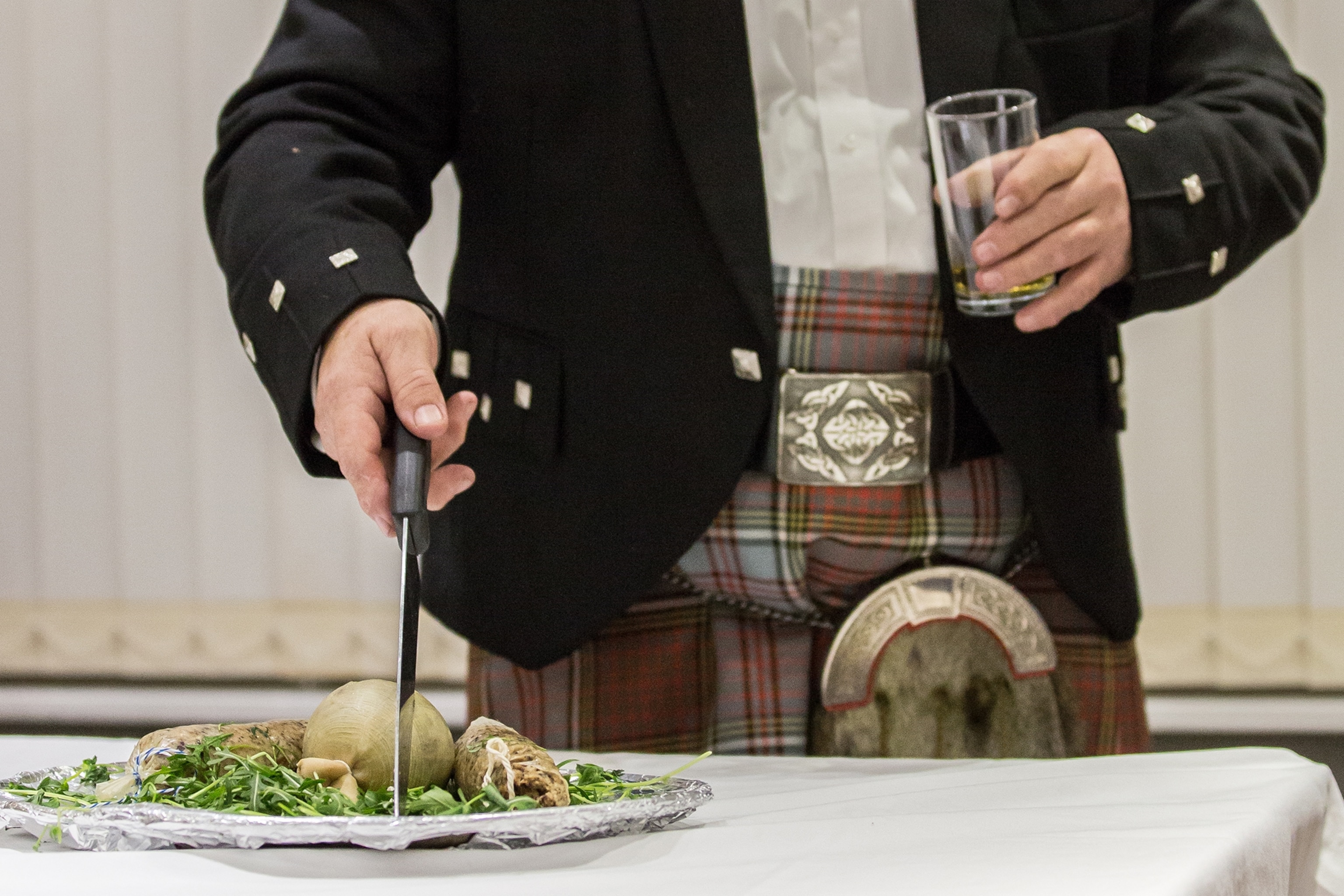A man in a traditional Scottish kilt ceremonially cuts cooked haggis on a plate