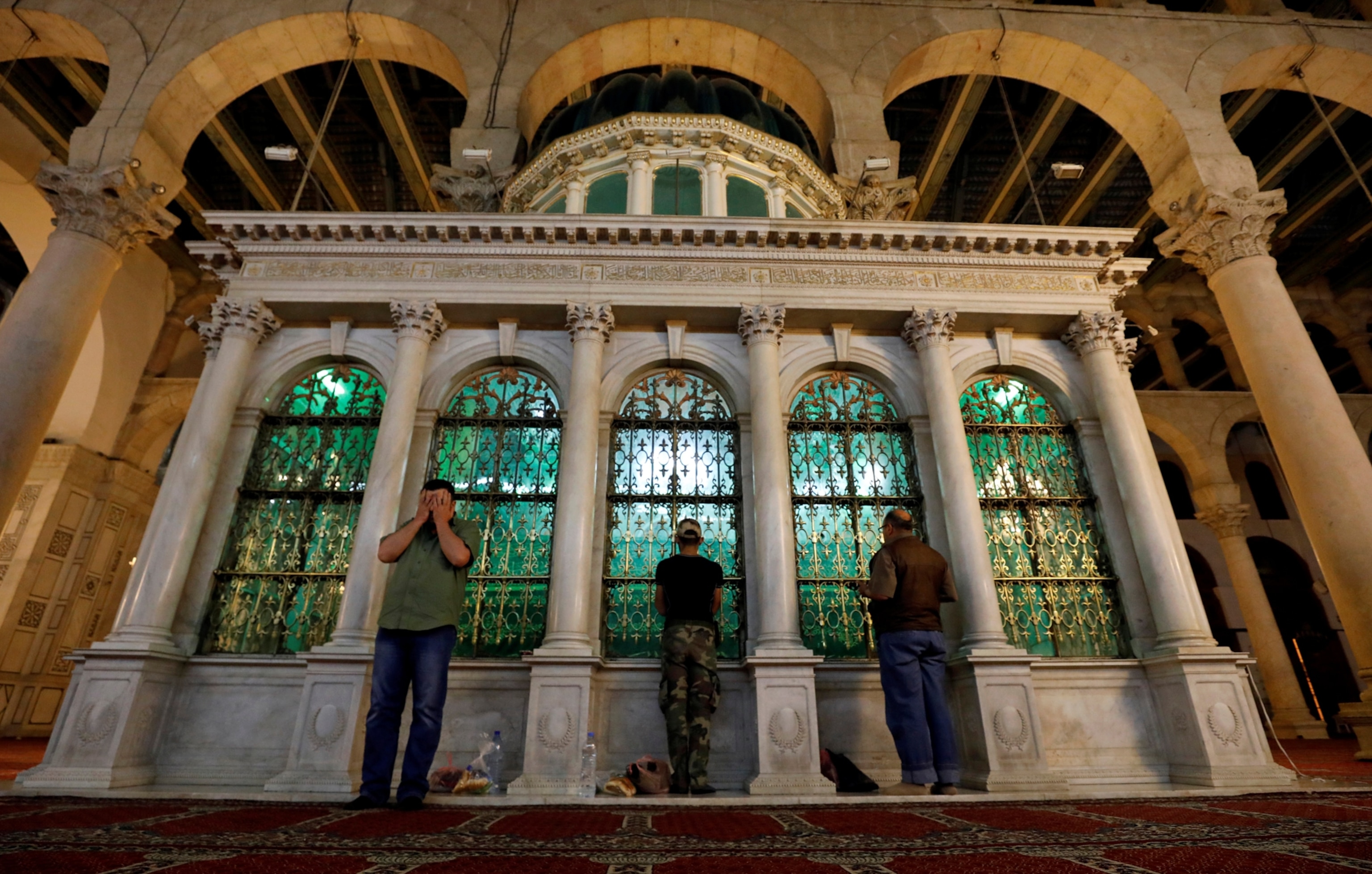 Three men standing in prayer before a white marble sepulcher containing a relic of John the Baptist.