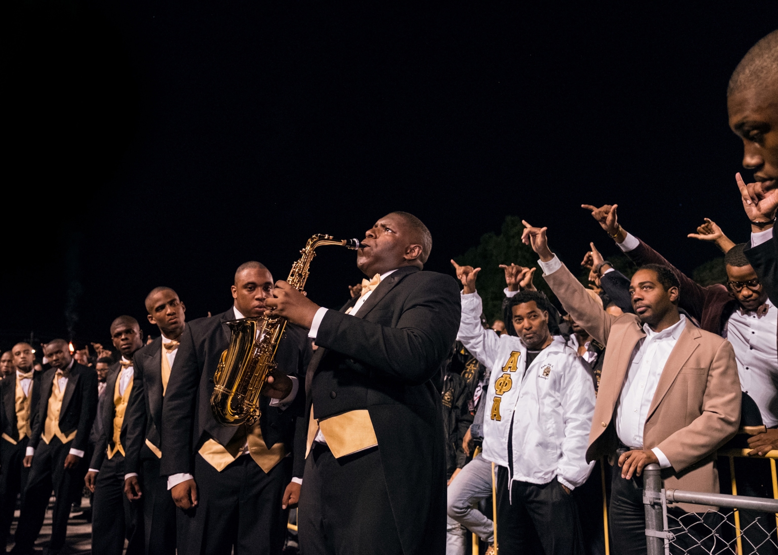 members of a fraternity club on stage as one leading man plays the saxophone