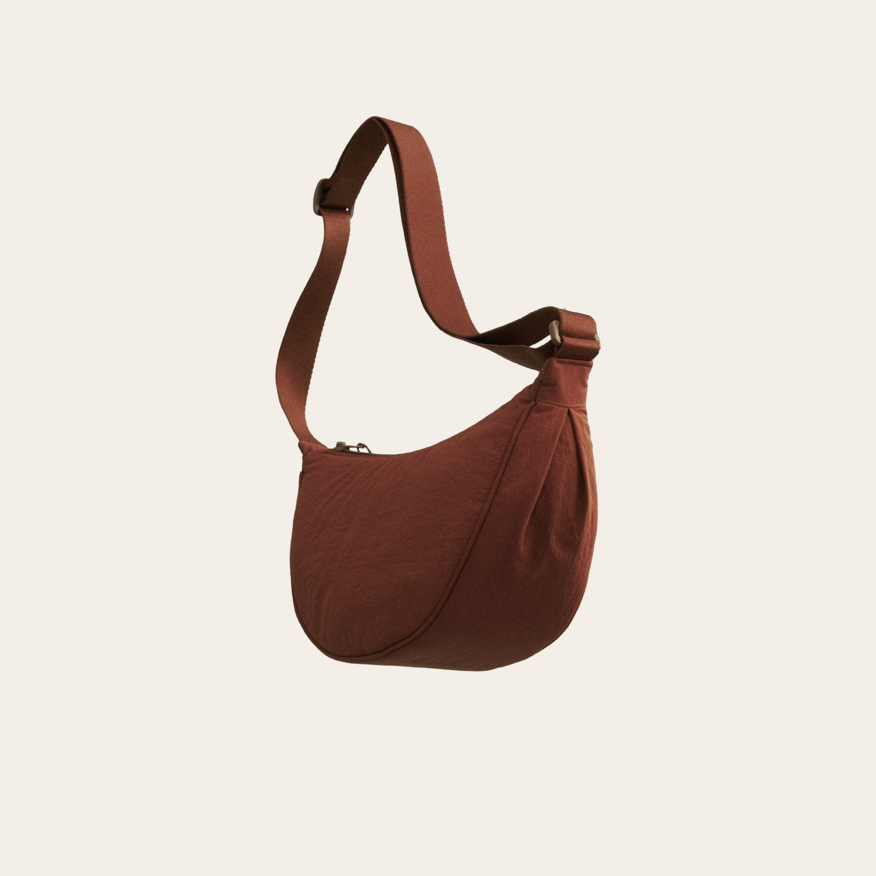 A one strapped bag with a umber color on a cream background.