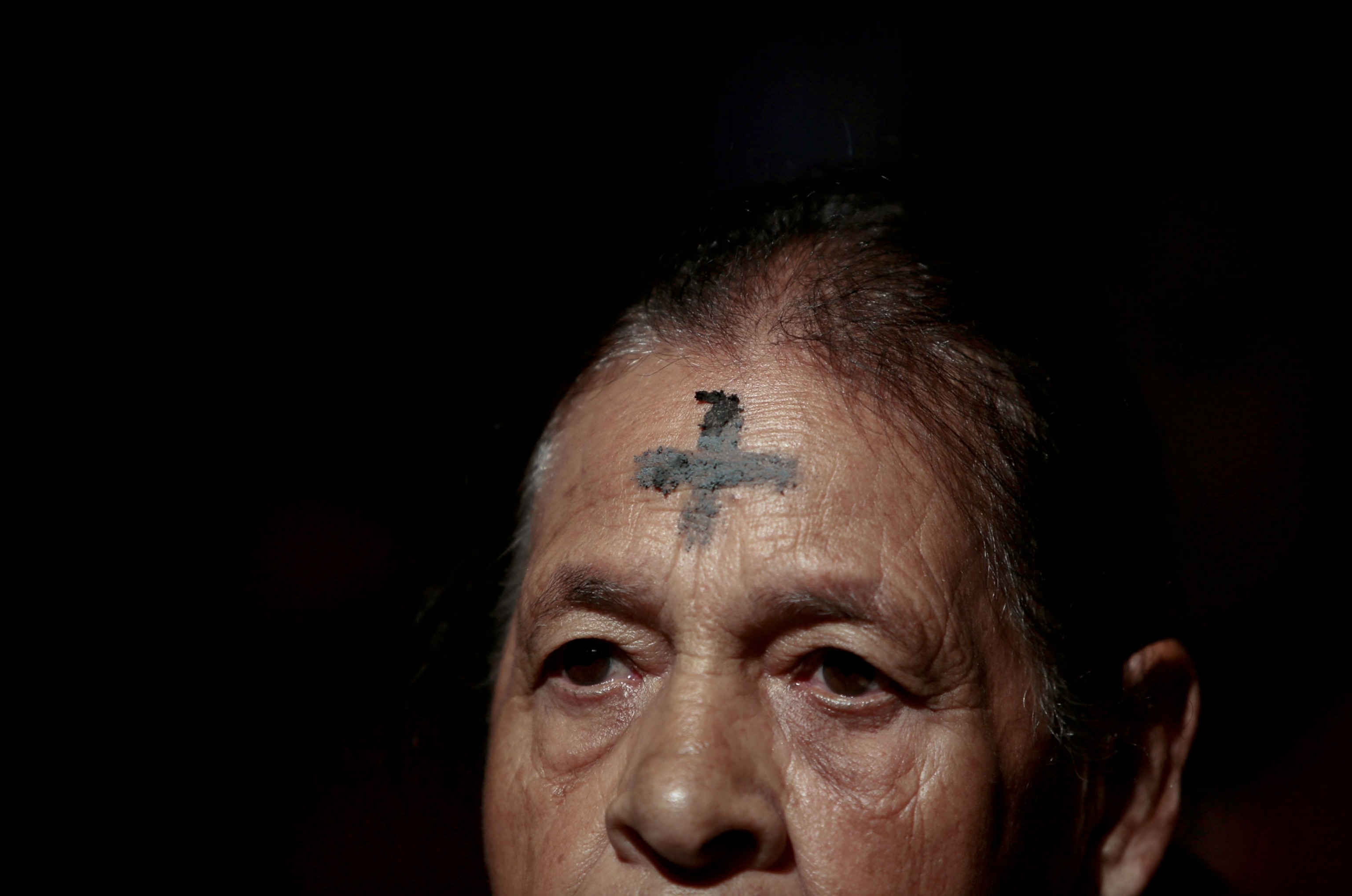 a woman with a cross of ashes is illuminated against a dark background