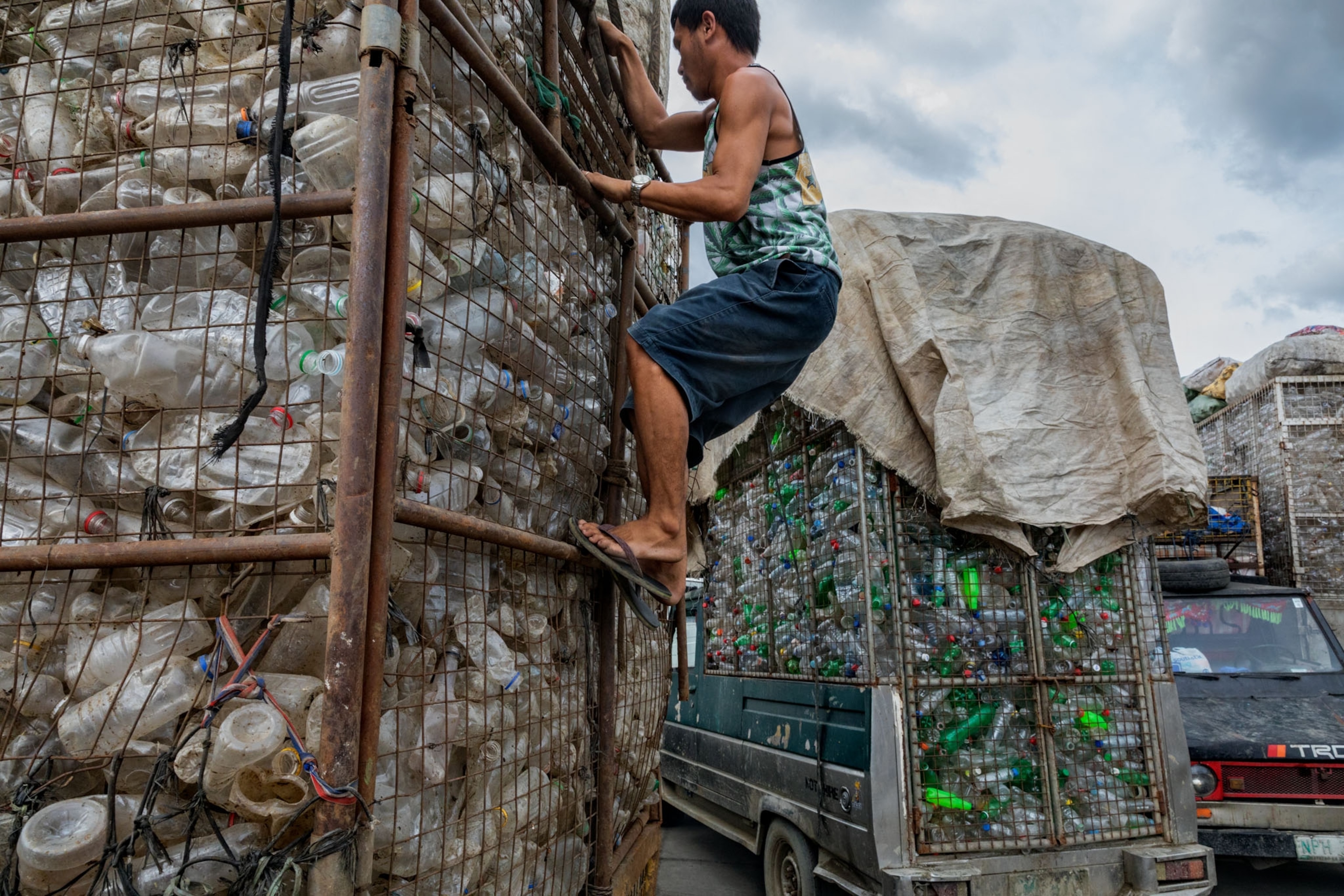 a man latching onto the side of a truck filled with plastic bottles
