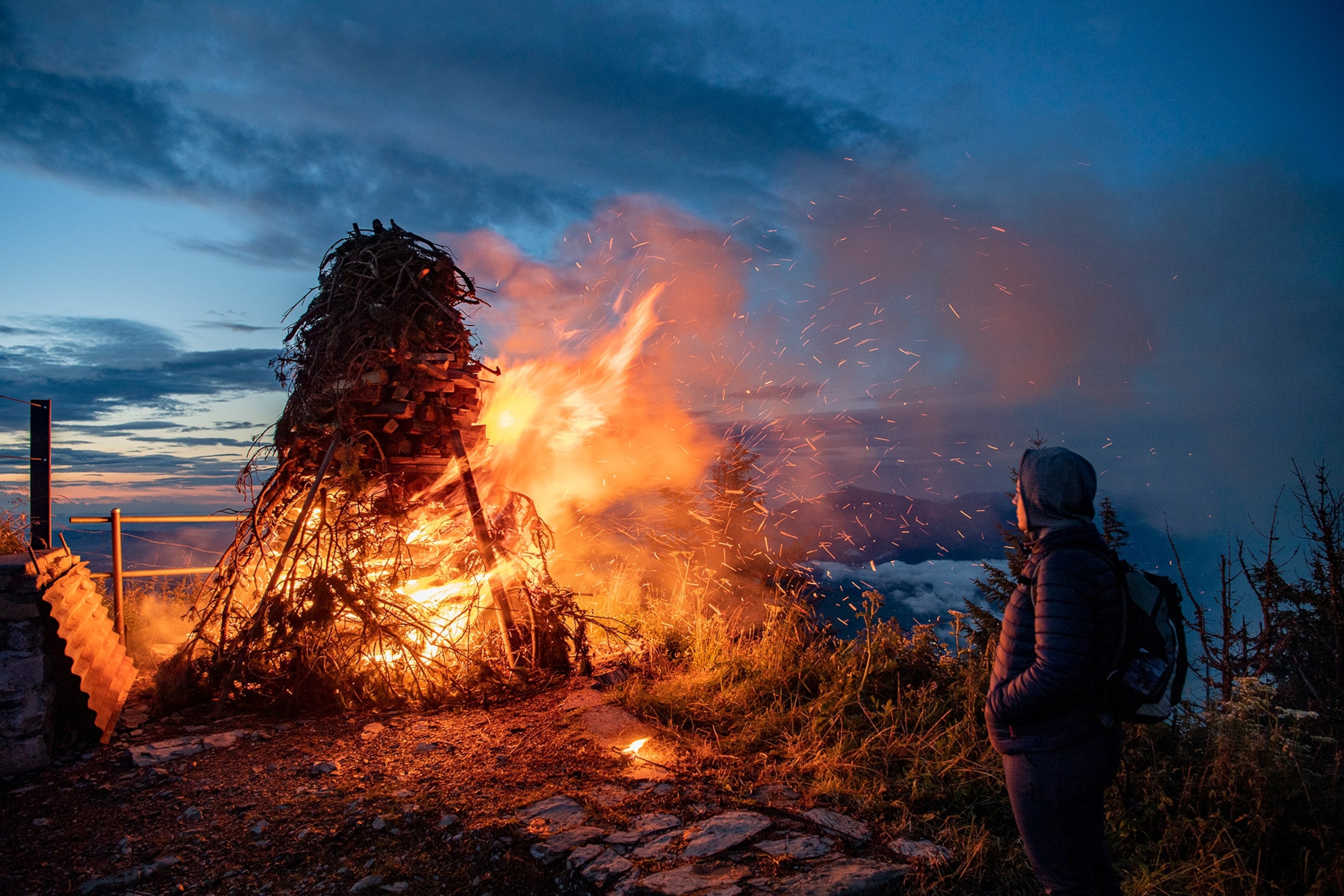 Warm light from a fire illuminates the area as a person watches.