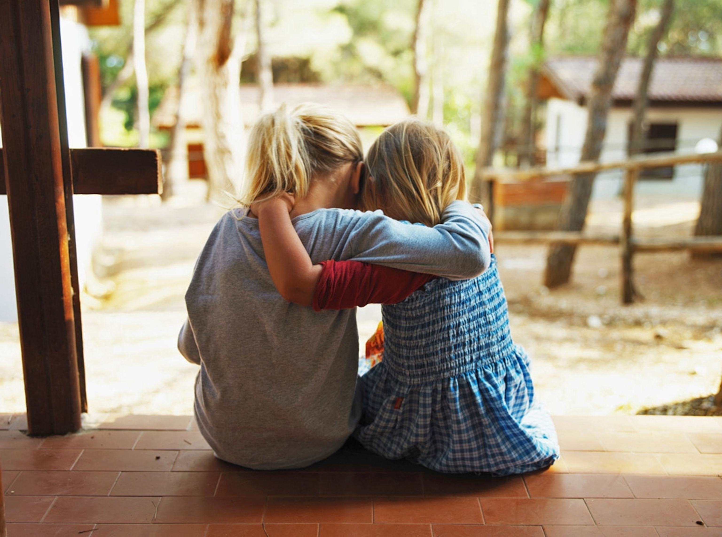 Two girls embracing on a porch, rear view. (No location given)