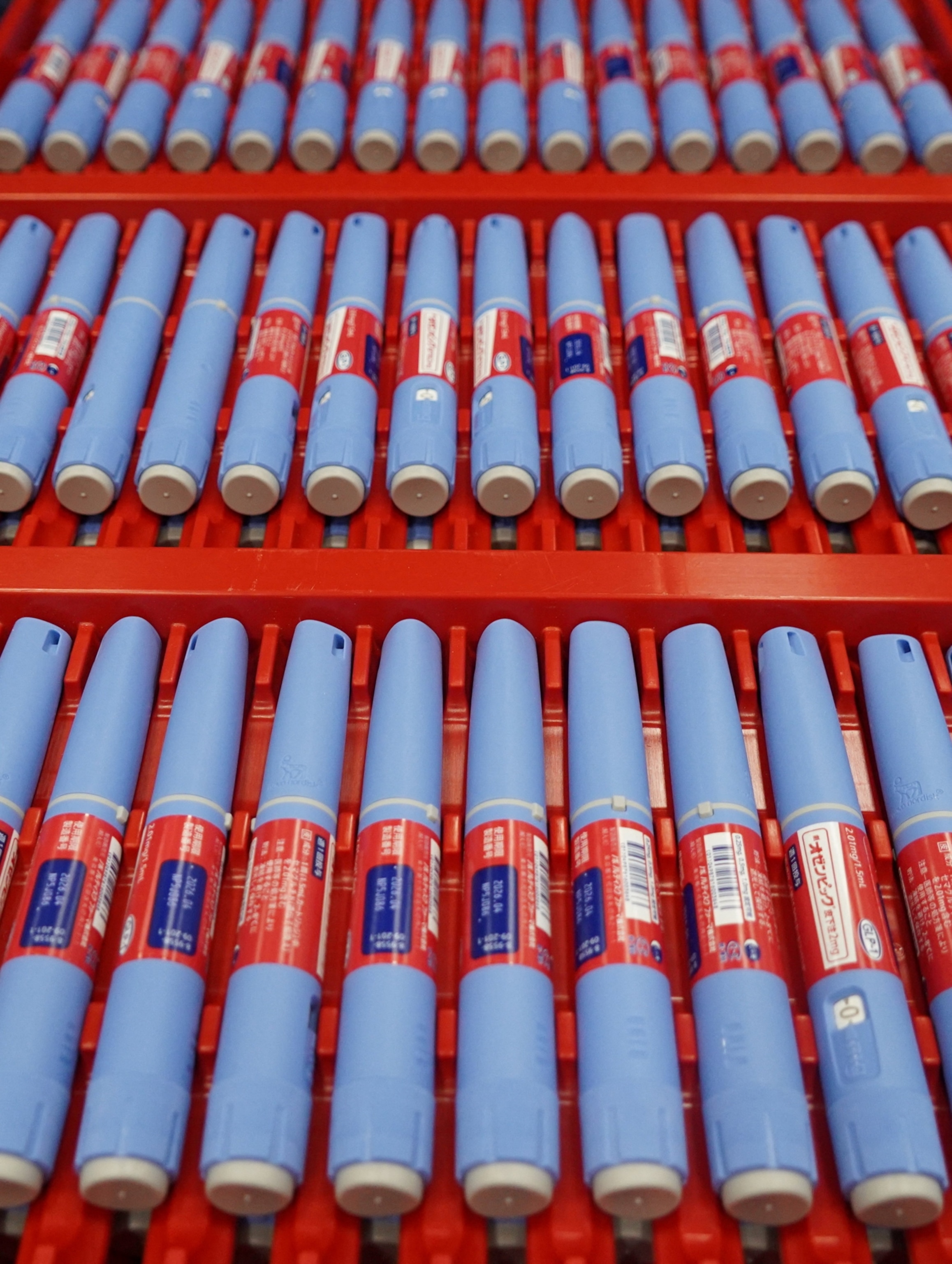 Rows of blue injection pens on a production line.
