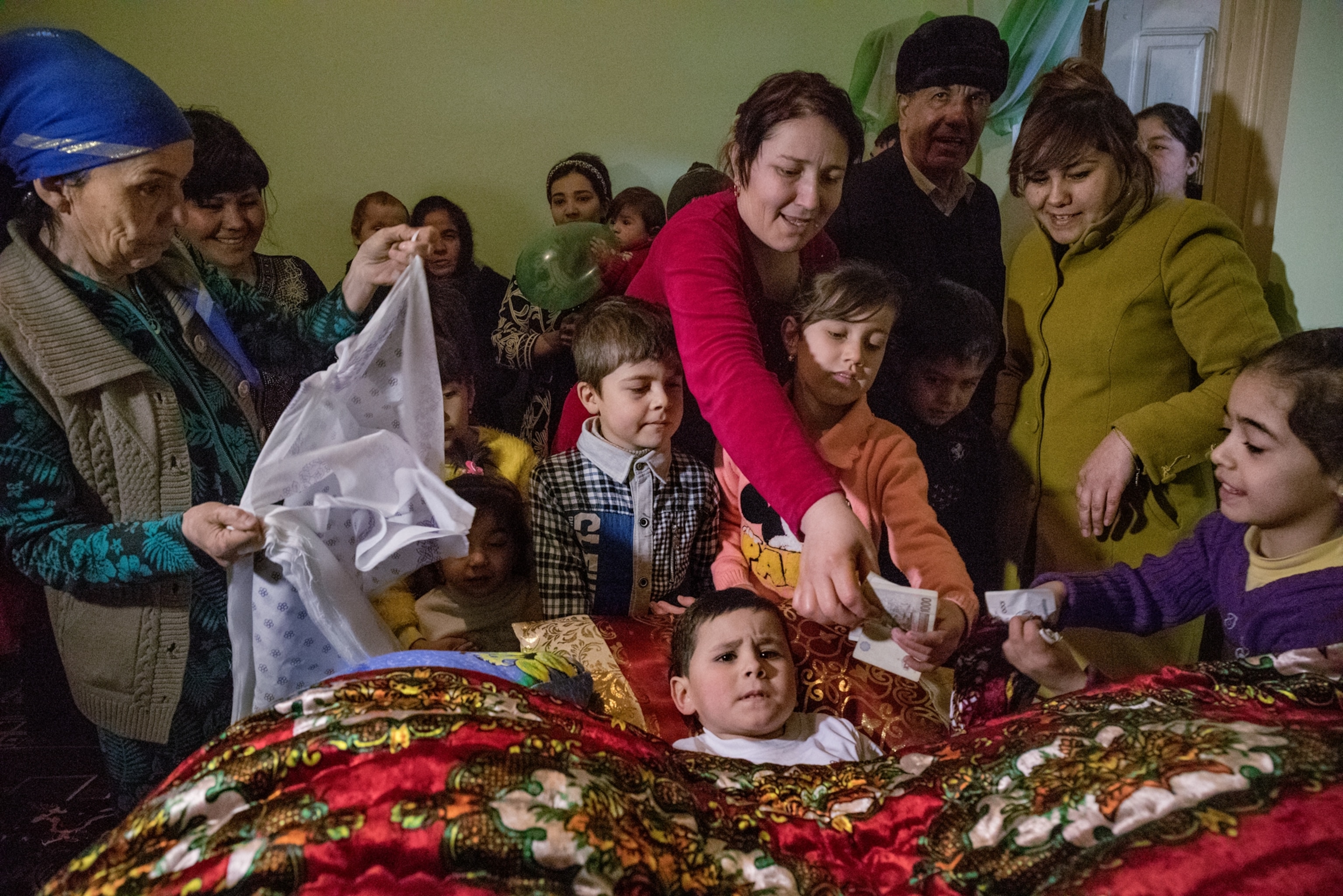 a large family surrounding a young boy during his circumcision ceremony in Uzbekistan