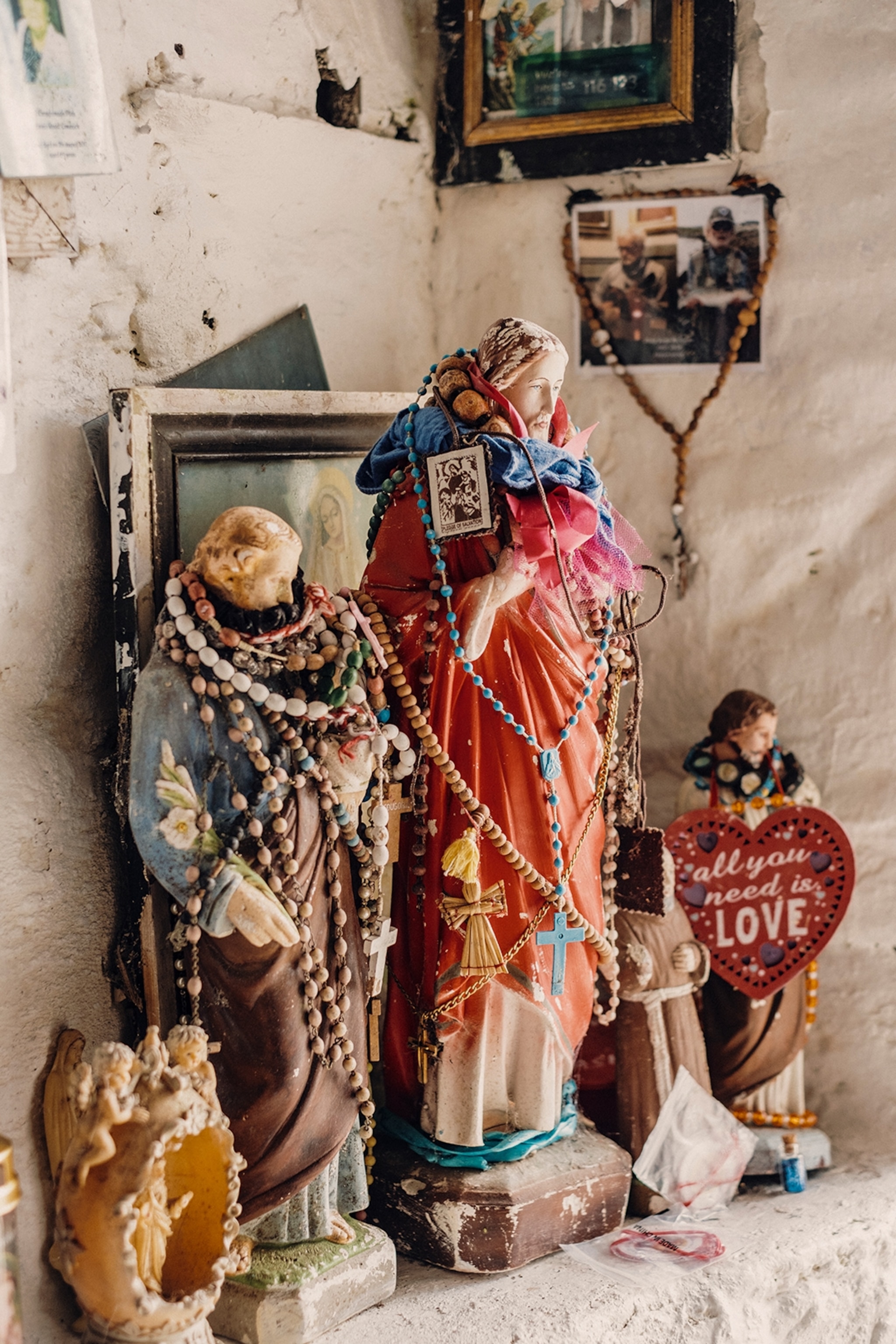 Figurines of saints strewn with colourful beads surrounded by photographs