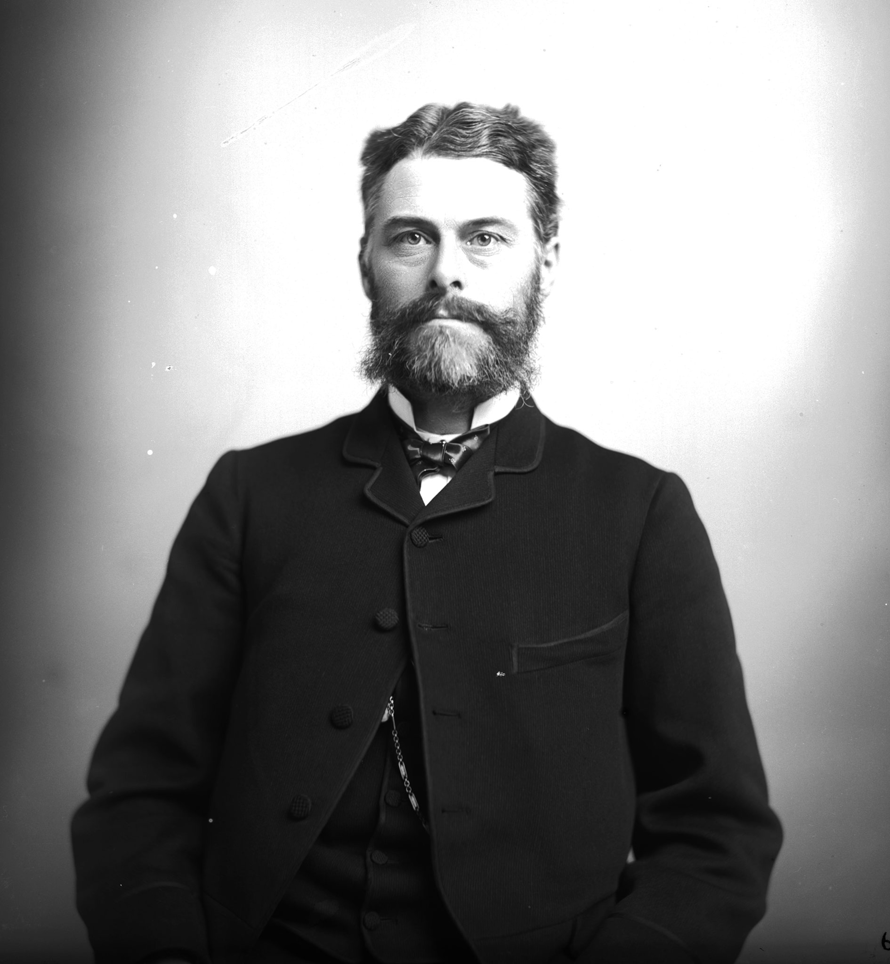 Black and white photograph of a portrait of a man with short, wavy hair, a beard, and dress attire from the late 1800s.